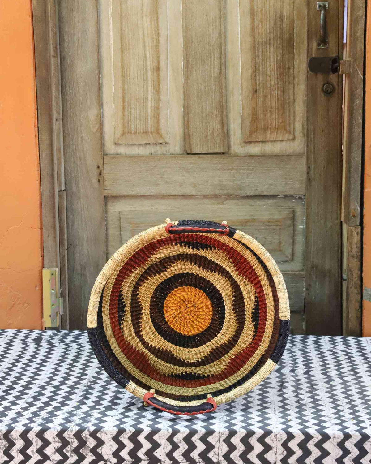 Handwoven Bolga wall tray disc in concentric red, black, yellow and natural bands with an orange centre.