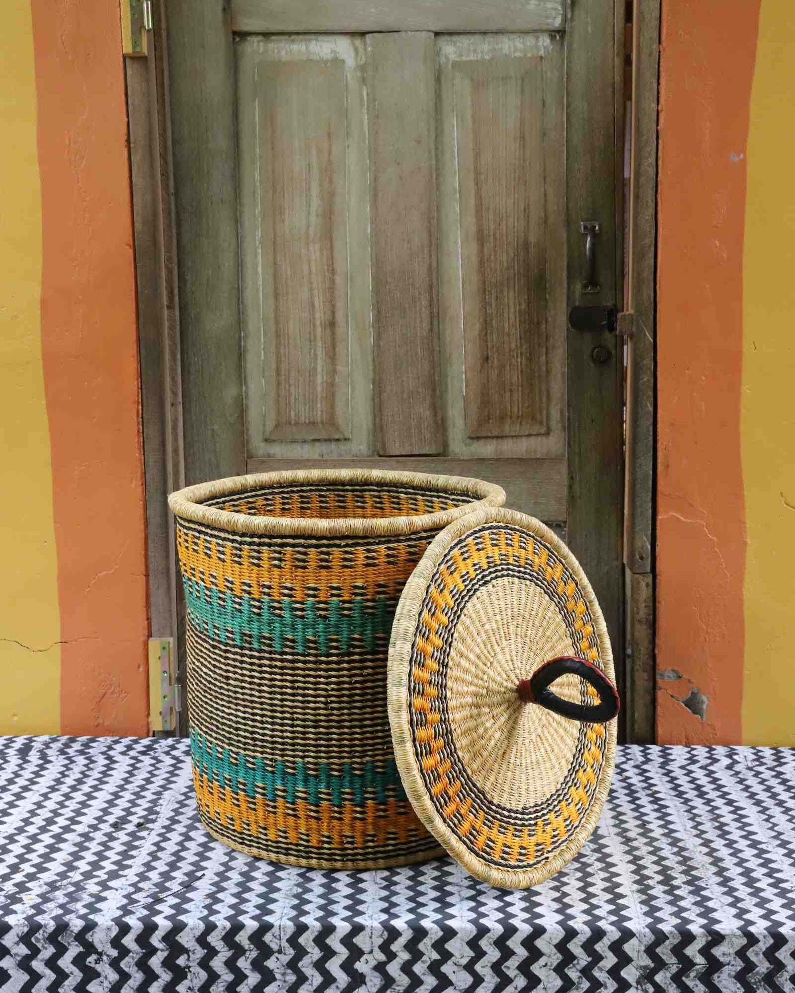 Handwoven Bolga laundry basket with lid removed, natural body with yellow-orange and teal stripes and lid.