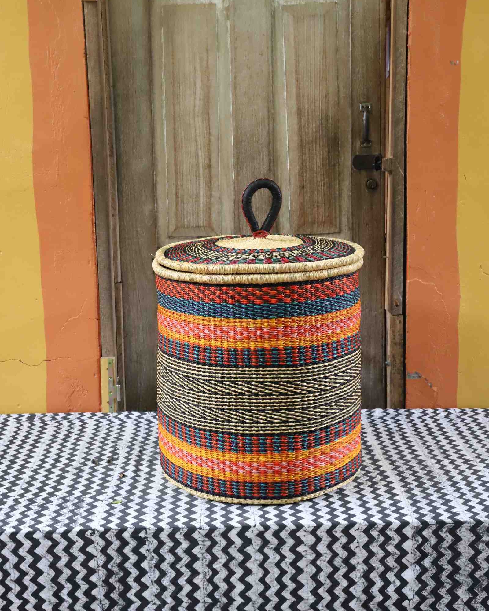 Large coiled-rim lidded laundry basket in rust, teal and gold striped weave, styled on a chevron cloth.
