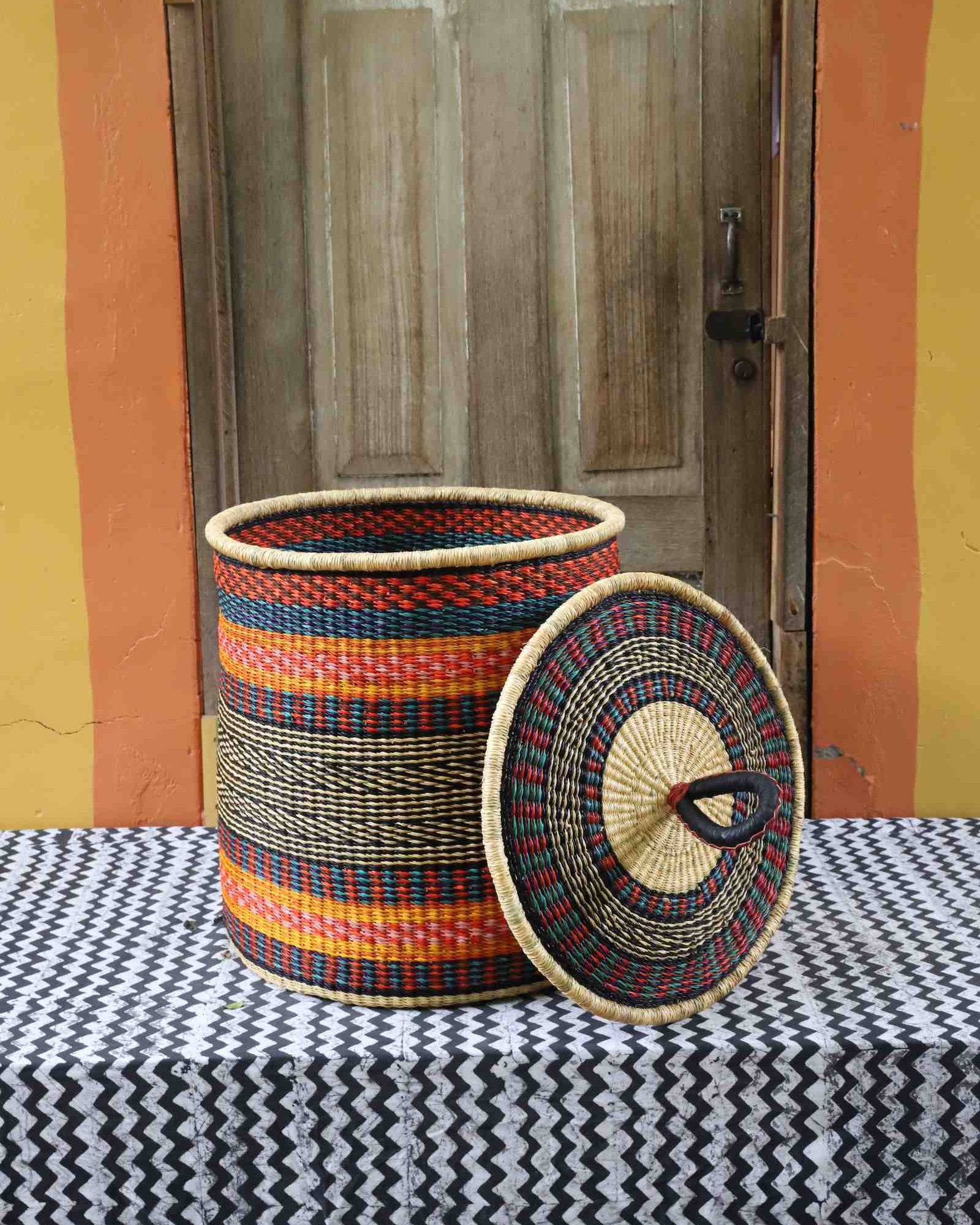Large coiled-rim laundry basket in rust, teal and gold striped weave, lid resting alongside on a chevron cloth.