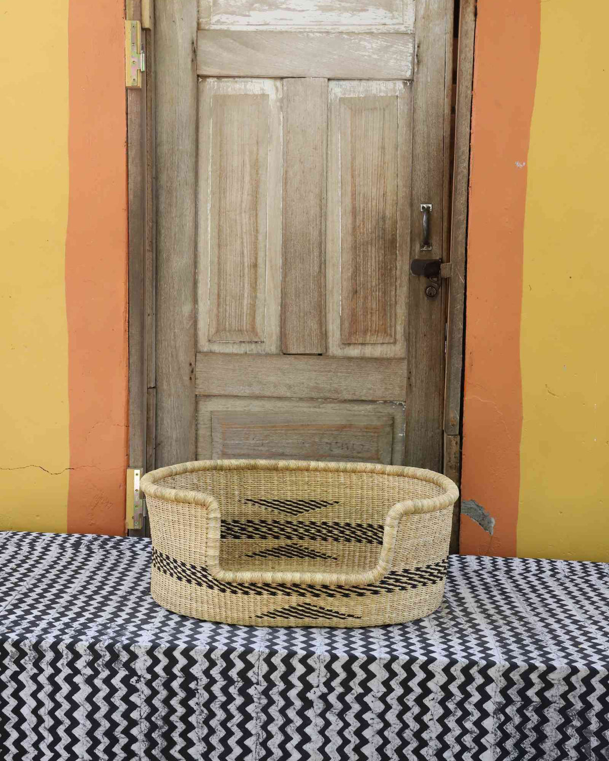 Small handwoven Bolga pet bed in natural straw with a subtle black arrow motif on the sides.