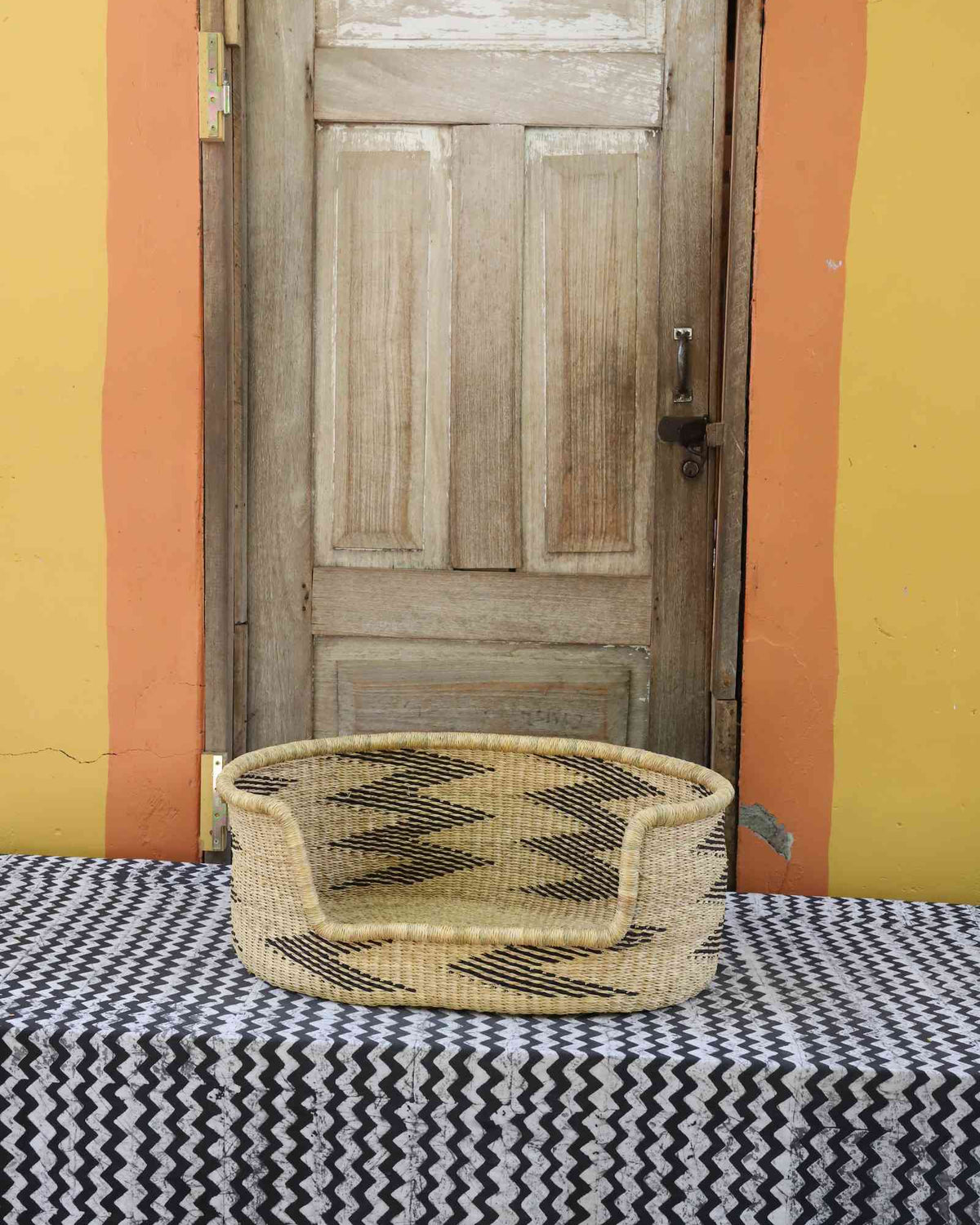 Large handwoven Bolga pet bed in natural straw with a repeating black arrow pattern along the sides.