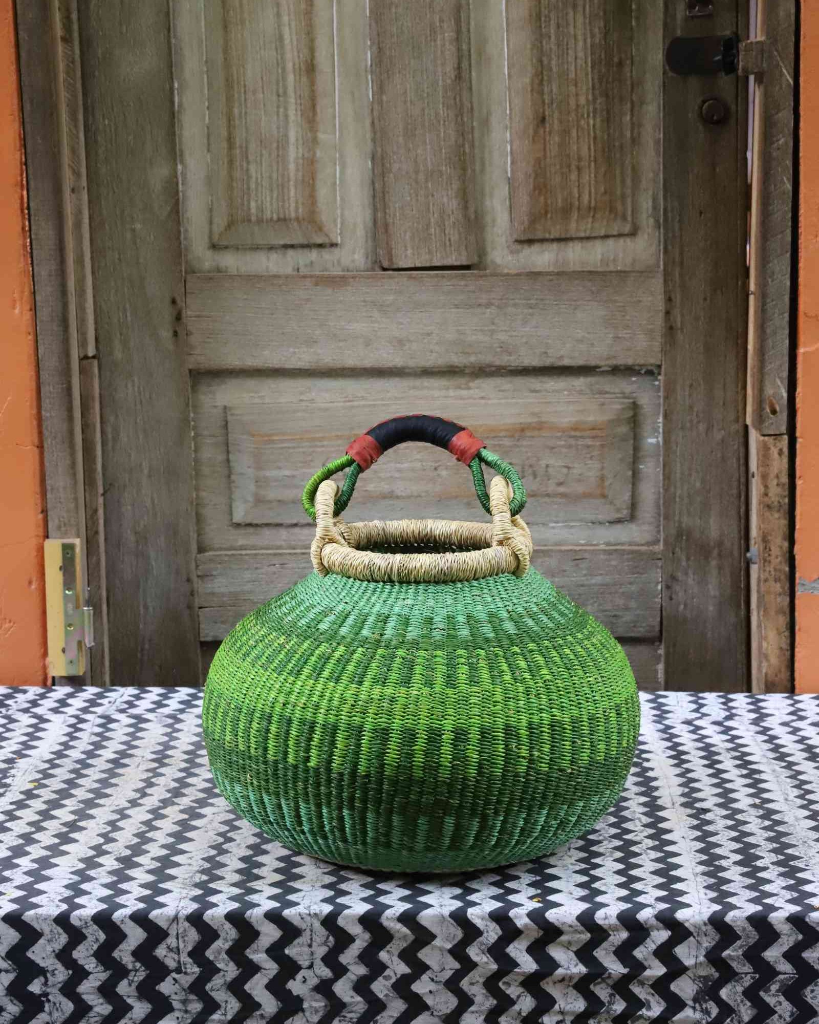 Large handwoven Bolga pot basket in lime green elephant grass with a leather top handle, on a chevron surface.