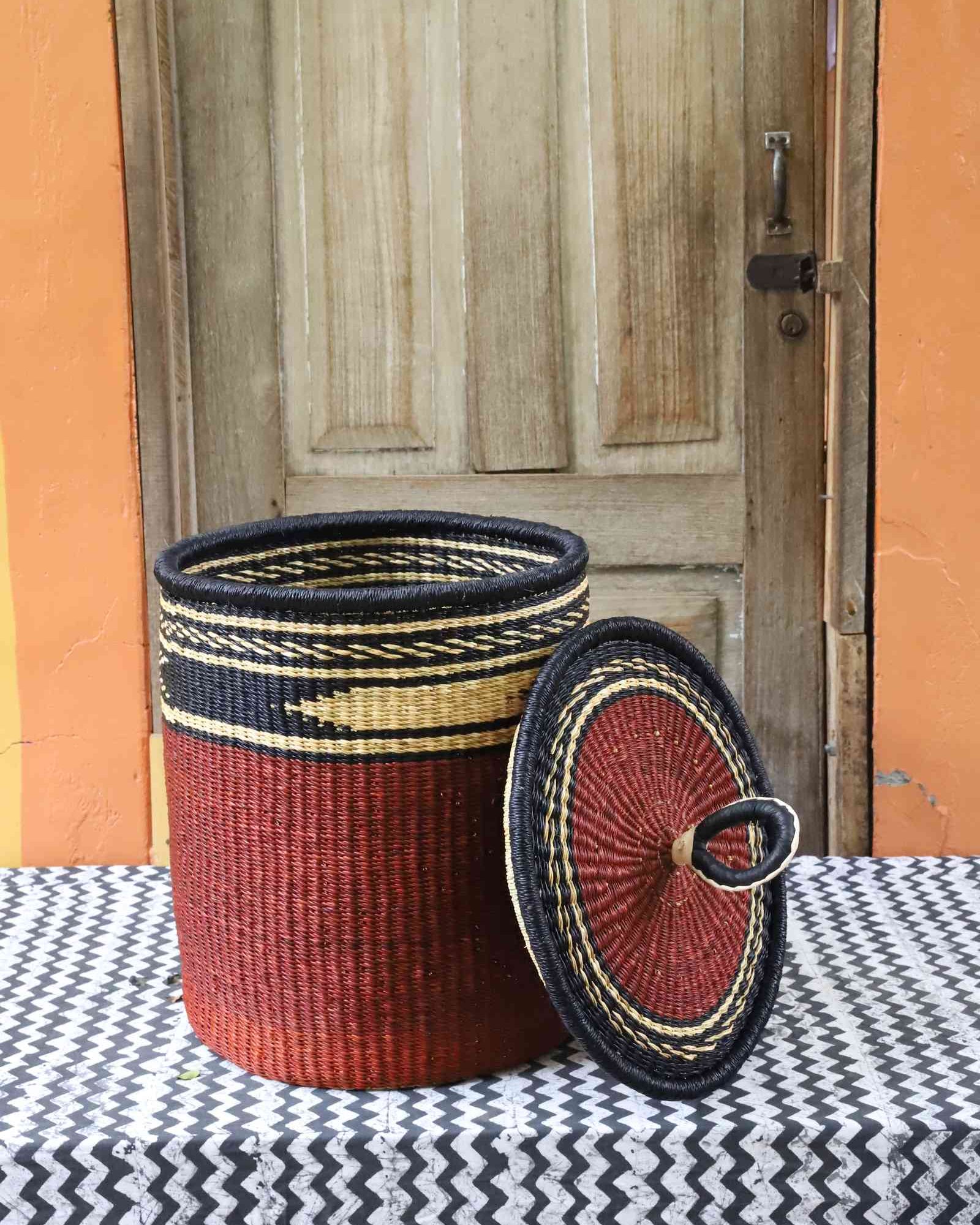 Coiled-rim laundry basket in solid rust weave, lid resting alongside on a chevron cloth.