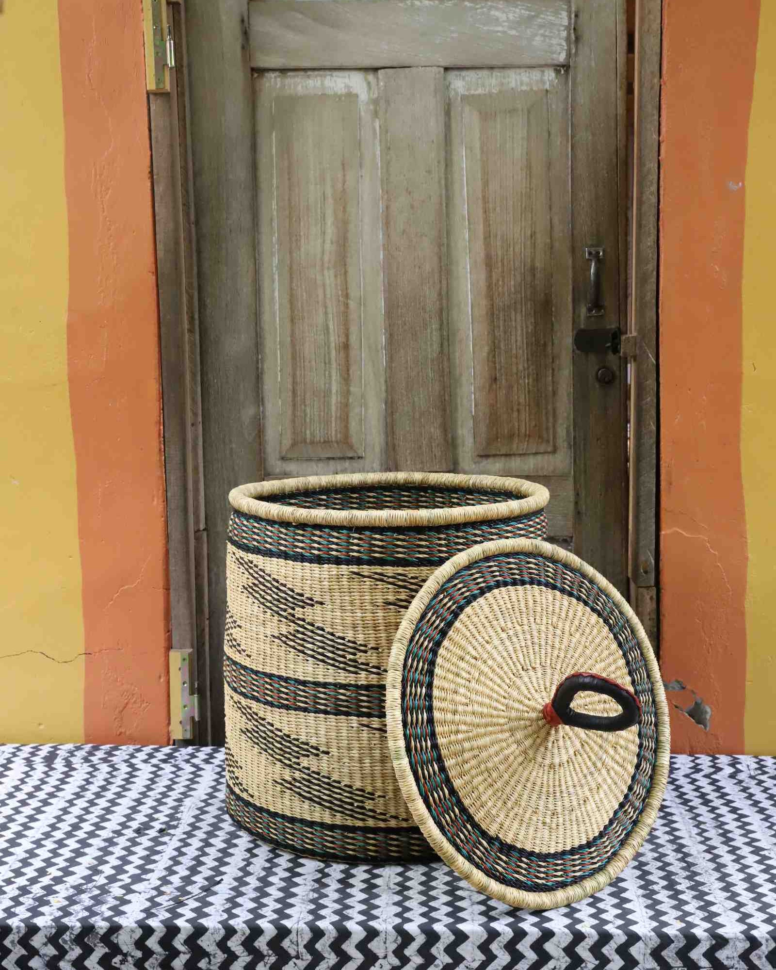 Handwoven Bolga laundry basket with lid removed, natural straw body with fine black banded wave motifs.