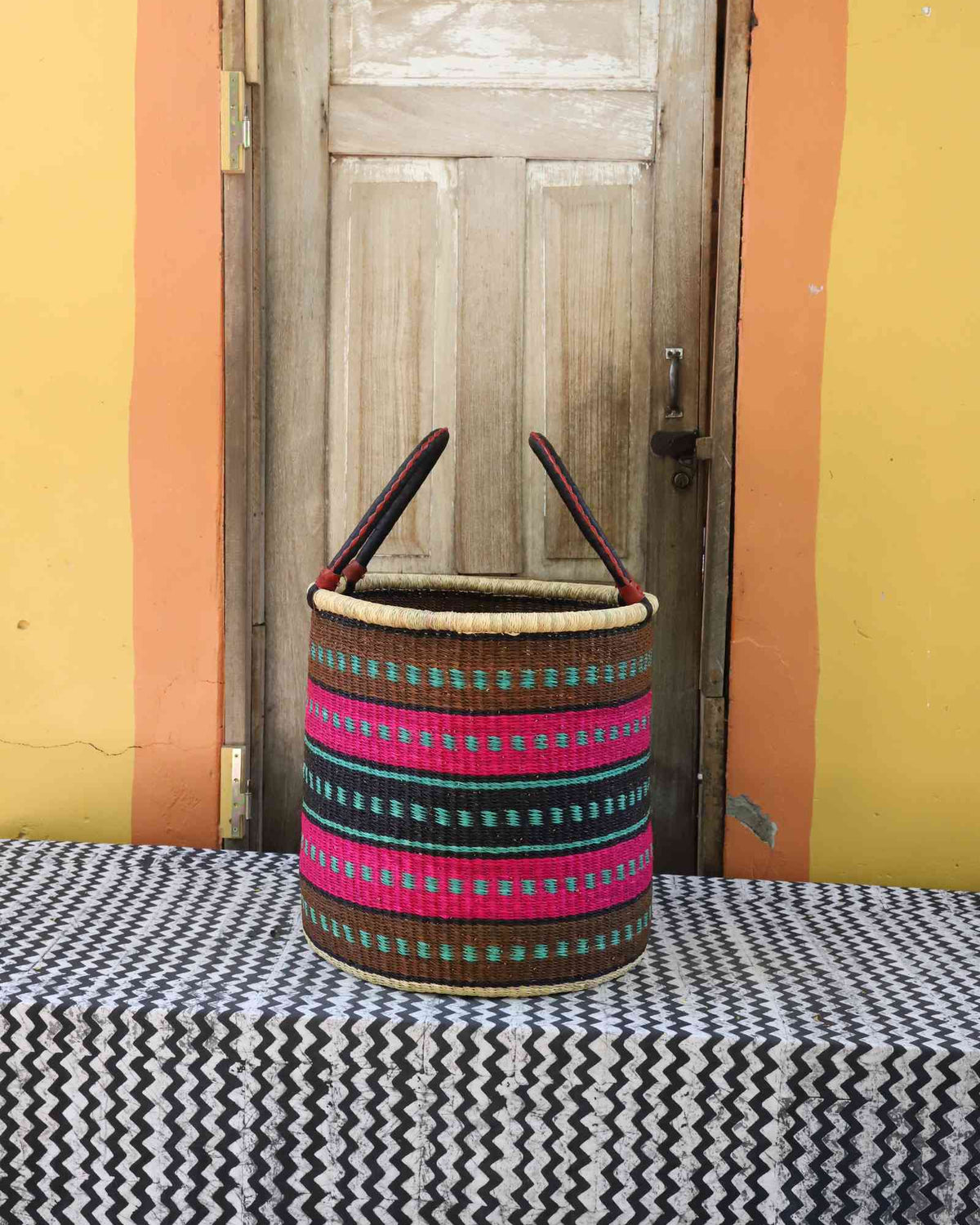 Large handwoven open-top Bolga laundry basket in natural straw with pink and dark banded stripes.