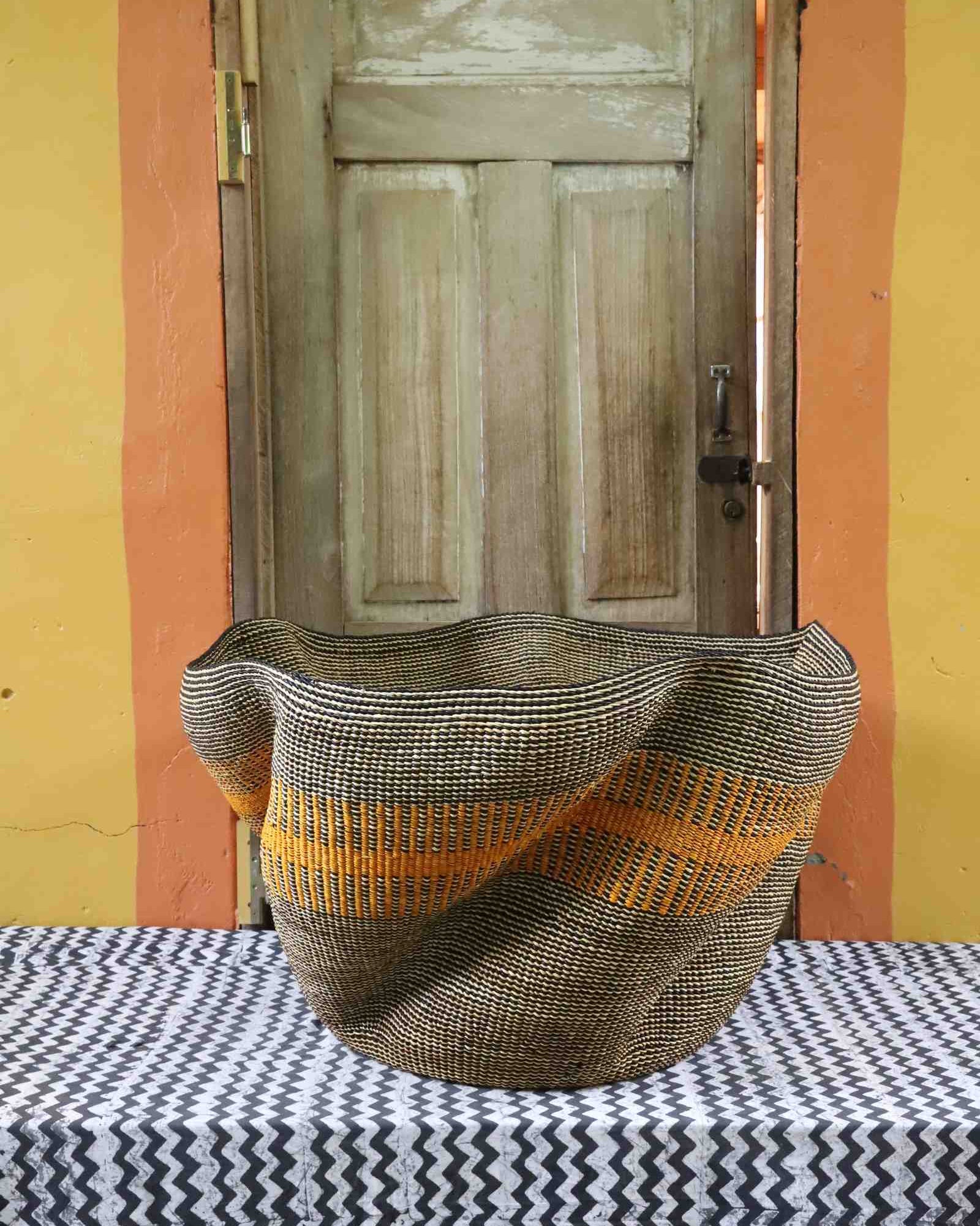Large sculptural Bolga basket with a wavy rim, woven in grey and natural tones with an orange stripe, on a tablecloth.