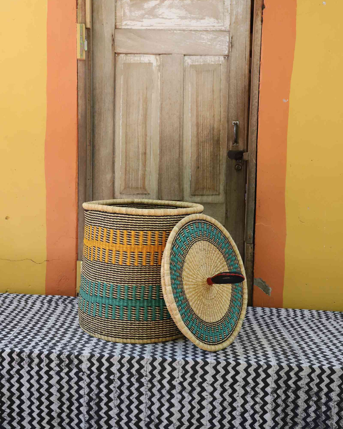 Handwoven Bolga laundry basket with lid removed, natural body with yellow and teal bands and matching lid.