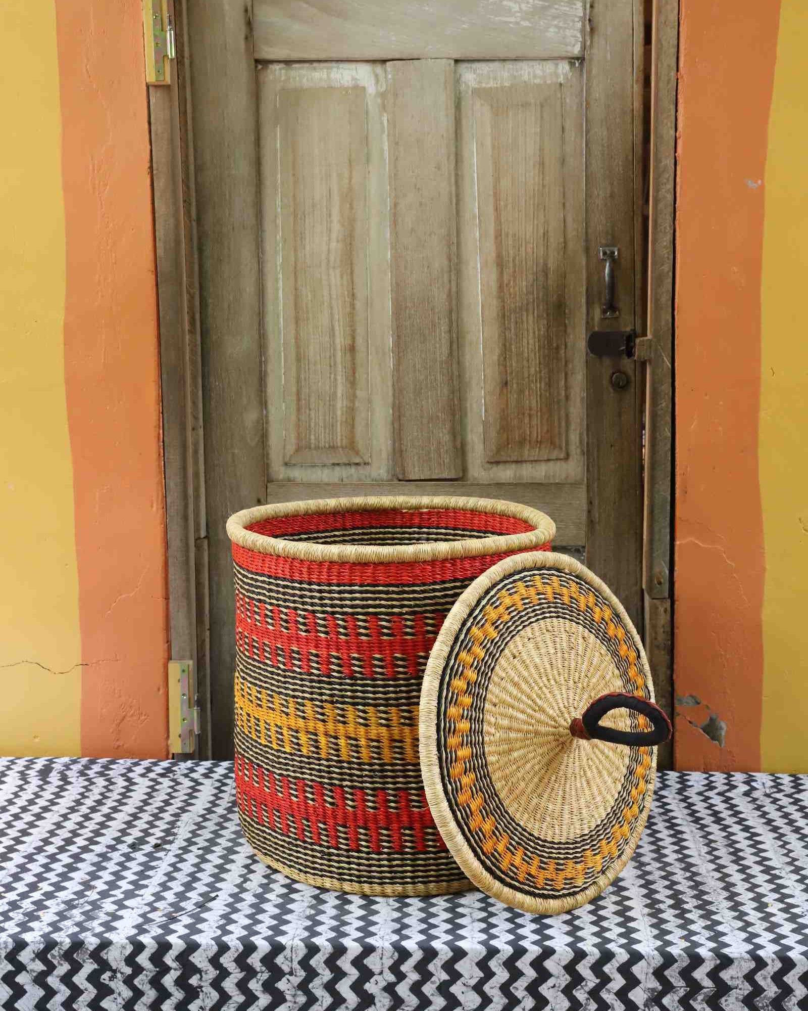 Handwoven Bolga laundry basket with lid removed, natural body with red, orange and yellow bands and matching lid.