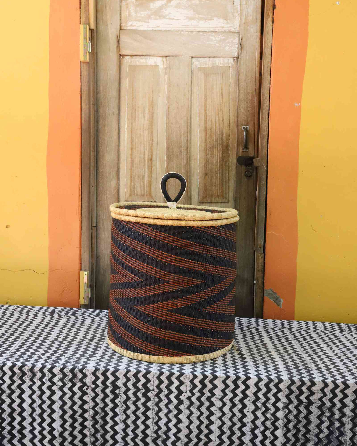 Handwoven Bolga laundry basket with coiled rim and lid in dark navy with rust-orange diagonal wave stripes.