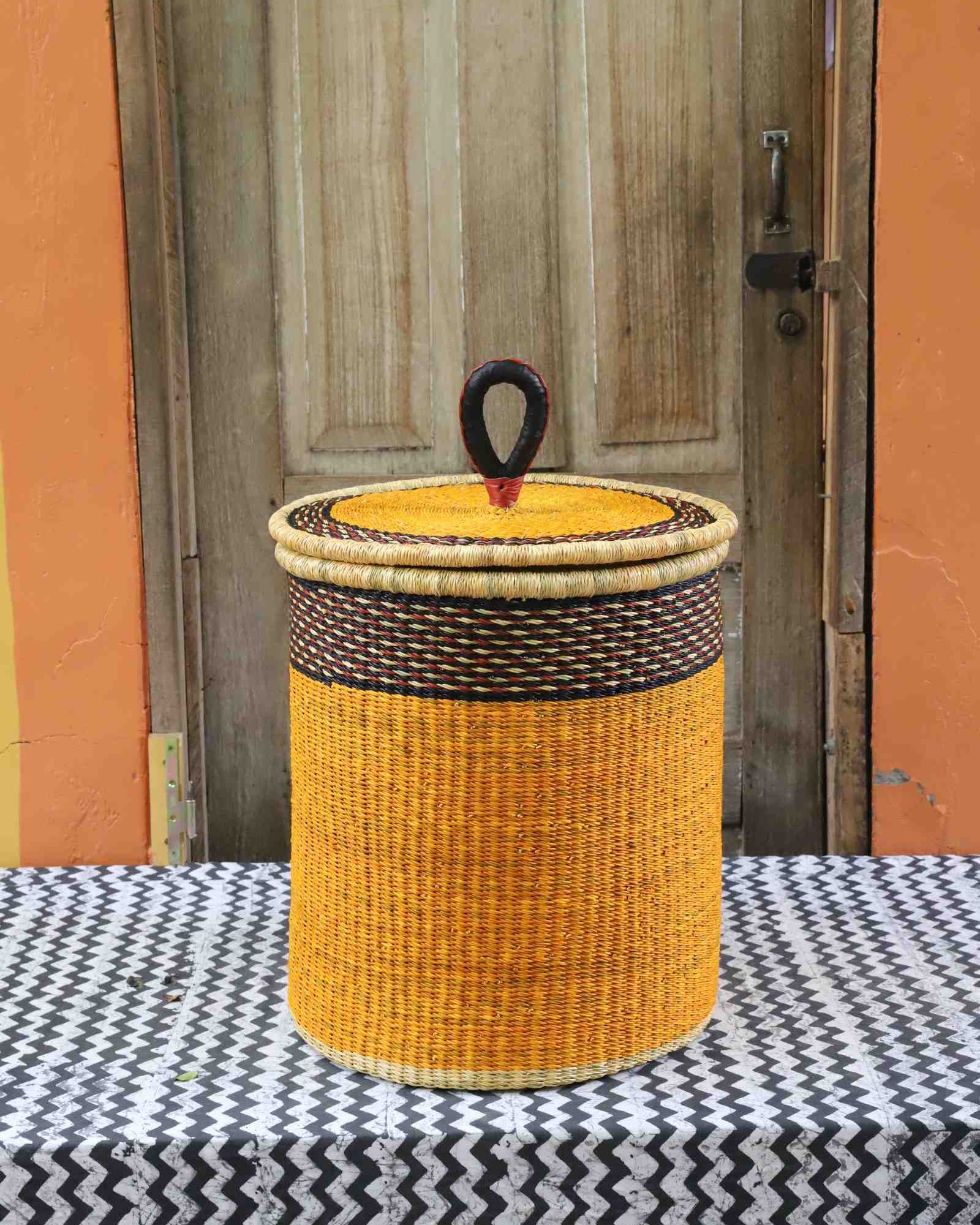 Coiled-rim lidded laundry basket in solid mustard weave with a black rim band, styled on a chevron cloth.