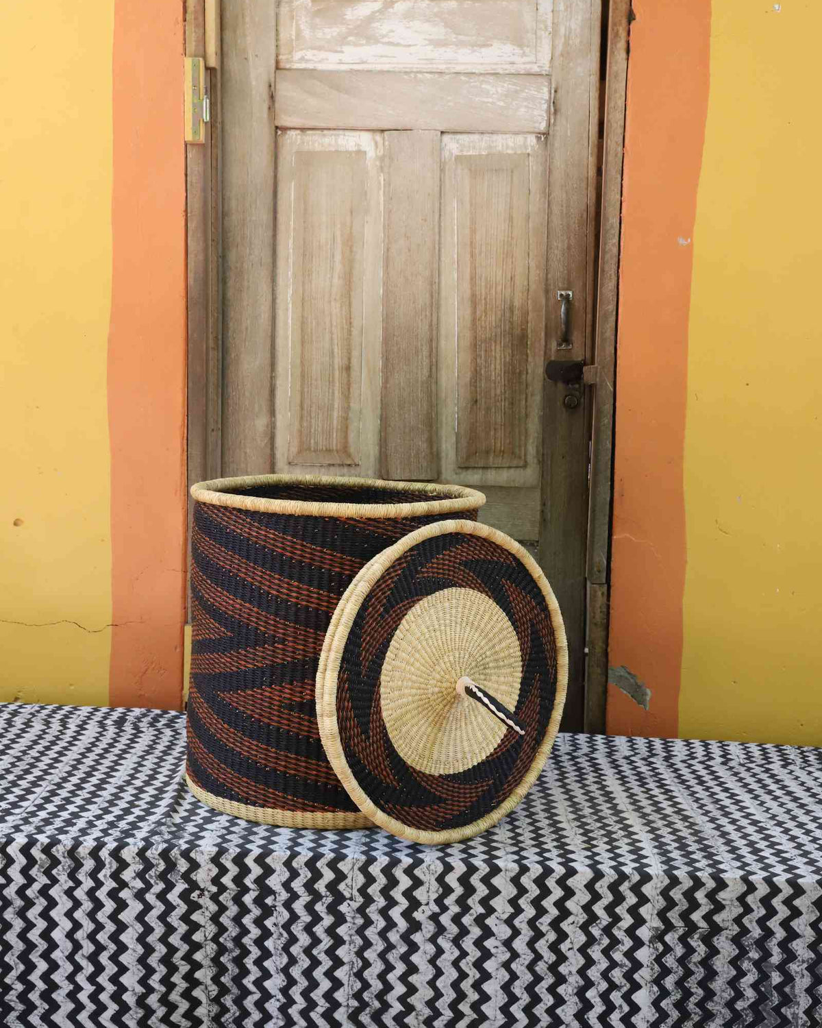 Handwoven Bolga laundry basket with lid removed, dark navy body with rust-orange waves and natural lid.