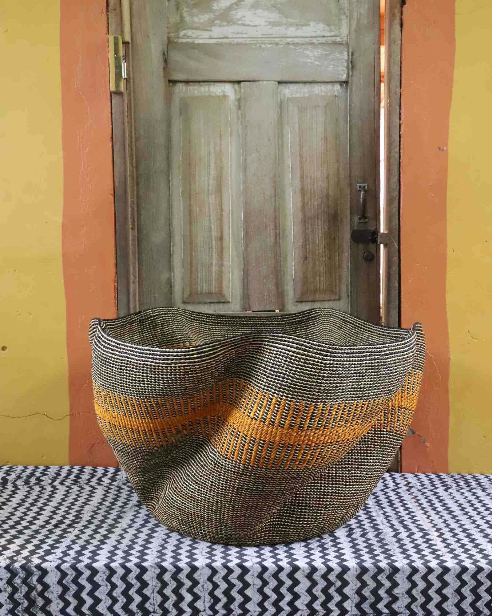 Sculptural Bolga basket with an undulating wavy rim, woven in grey and natural tones with an orange stripe band.