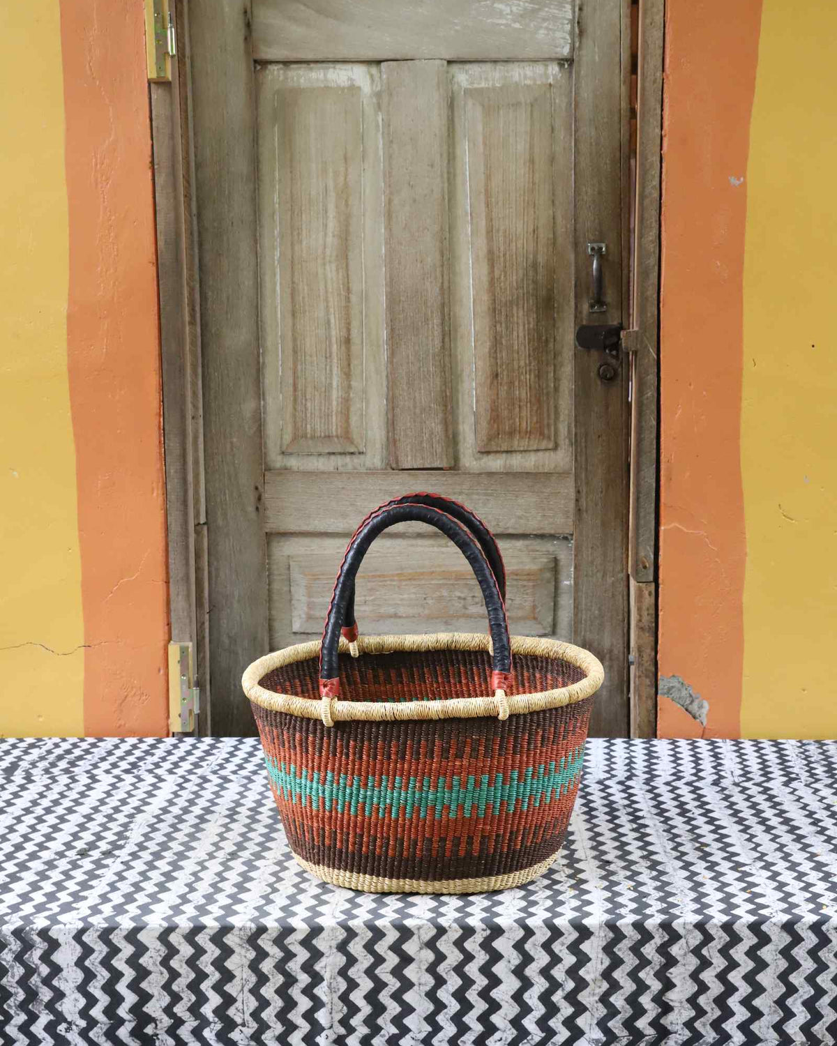 Medium handwoven oval Bolga shopping basket in natural straw with orange and teal banded stripes.
