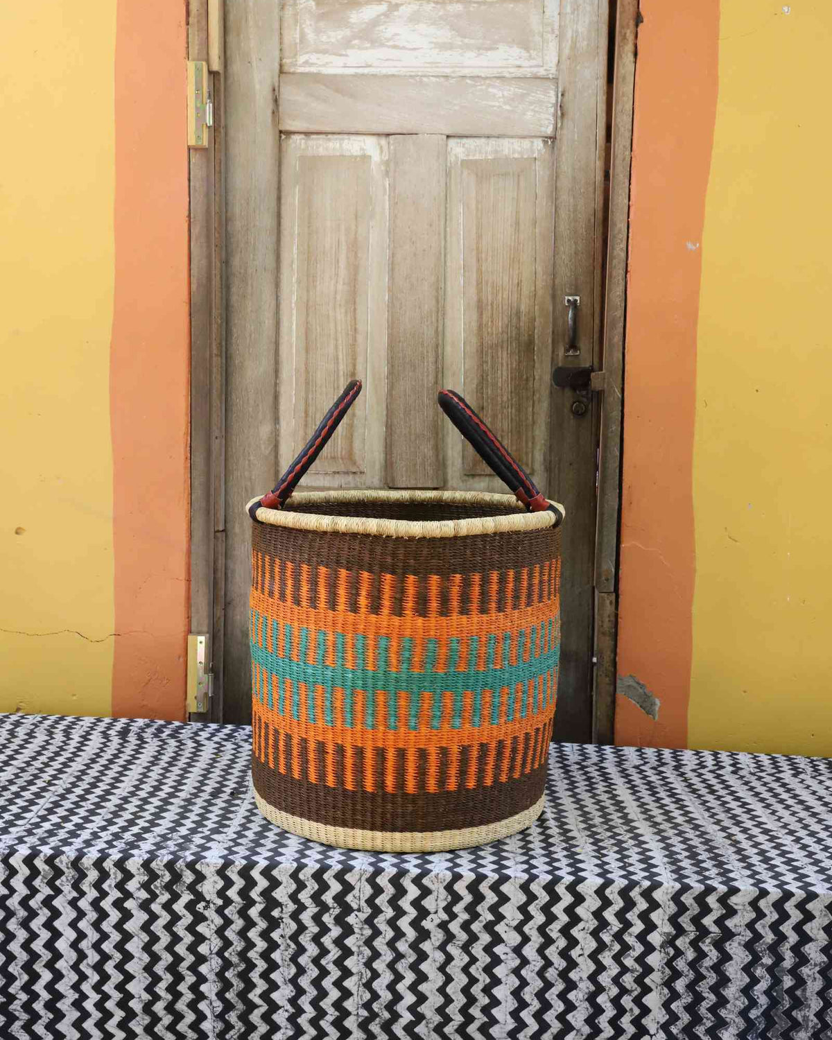 Large handwoven open-top Bolga laundry basket in brown, orange and teal banded stripes.
