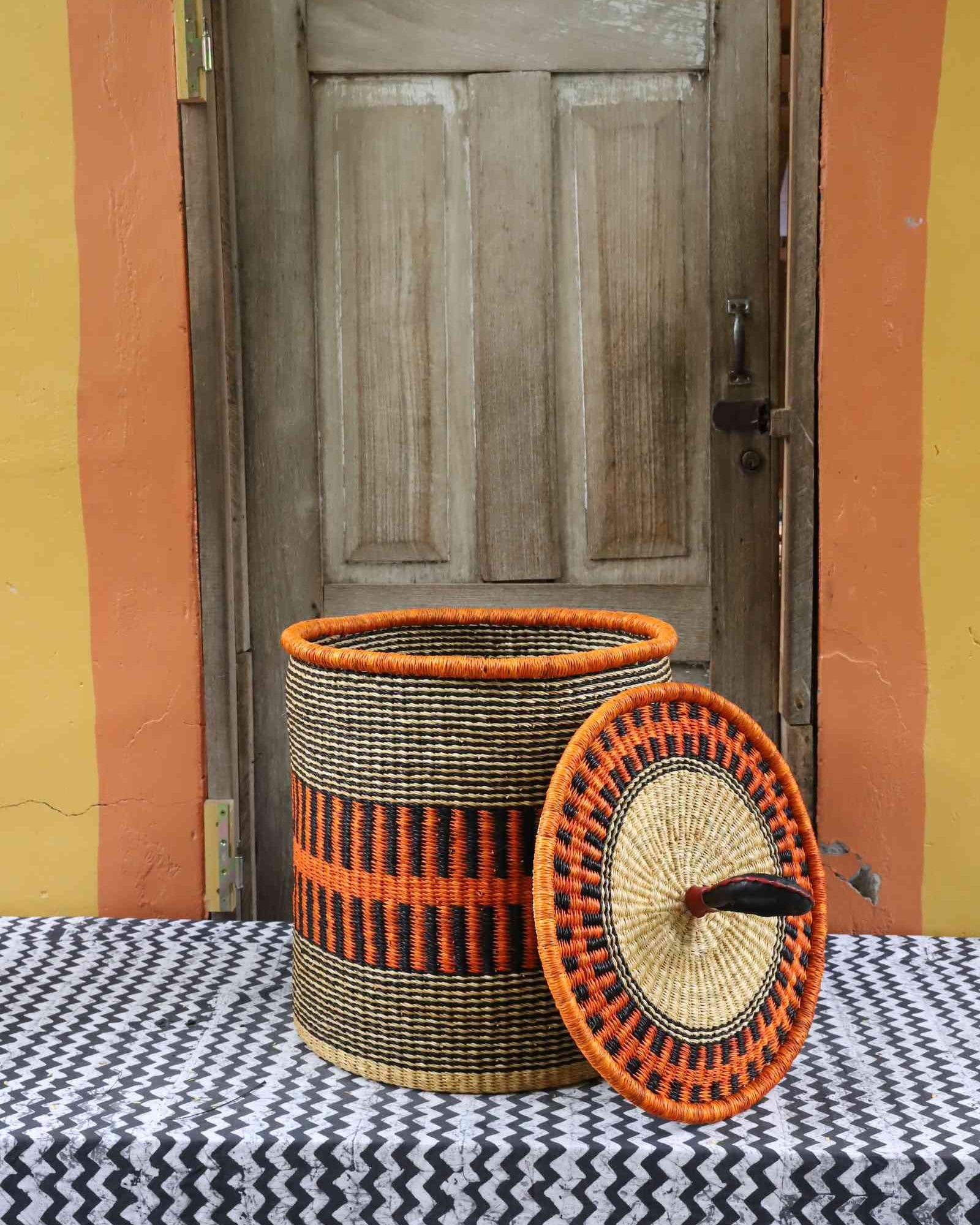 Handwoven Bolga laundry basket with coiled rim and lid removed, natural straw body with orange band.