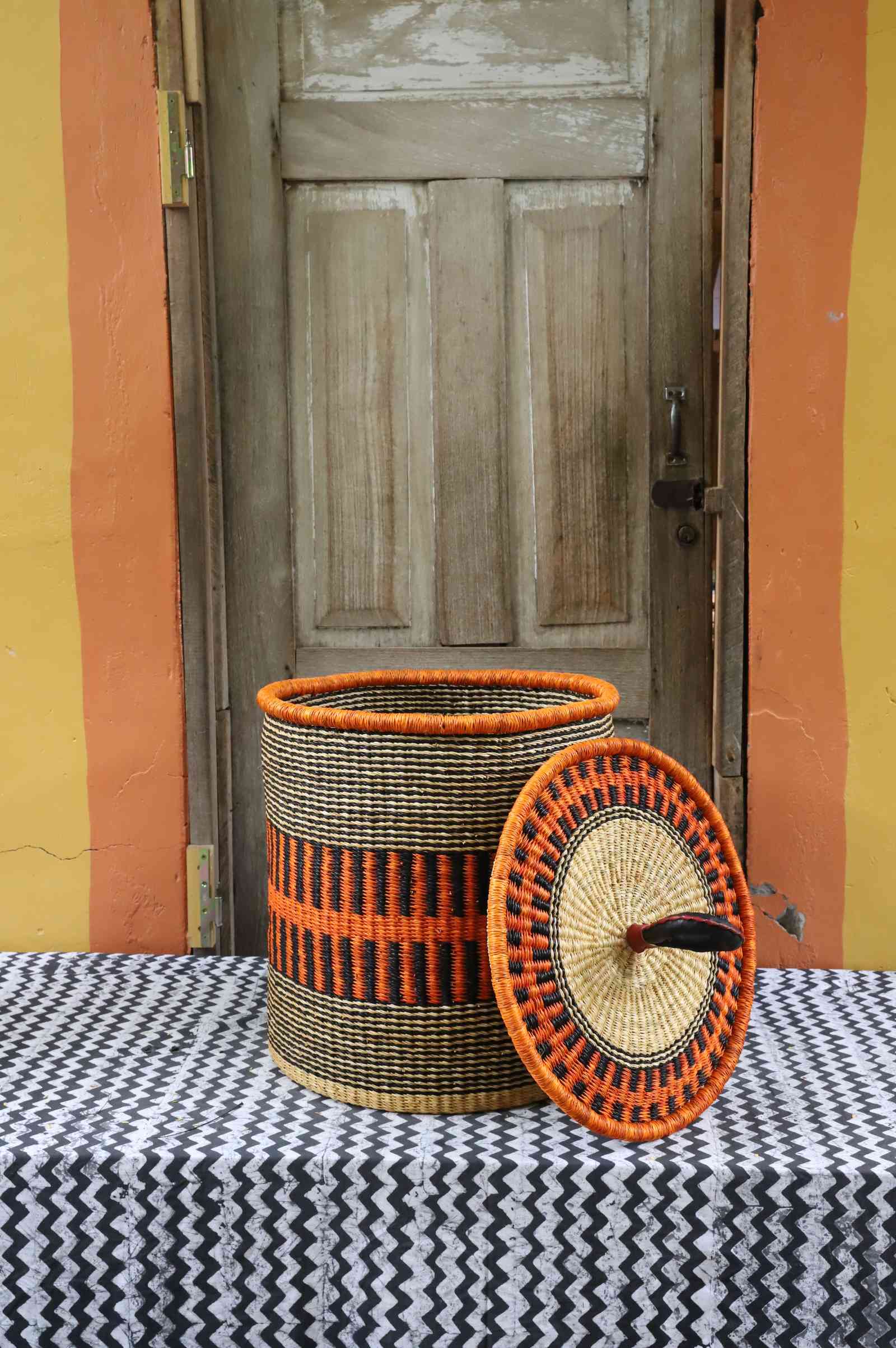 Handwoven Bolga laundry basket with coiled rim and lid removed, natural straw body with orange band.