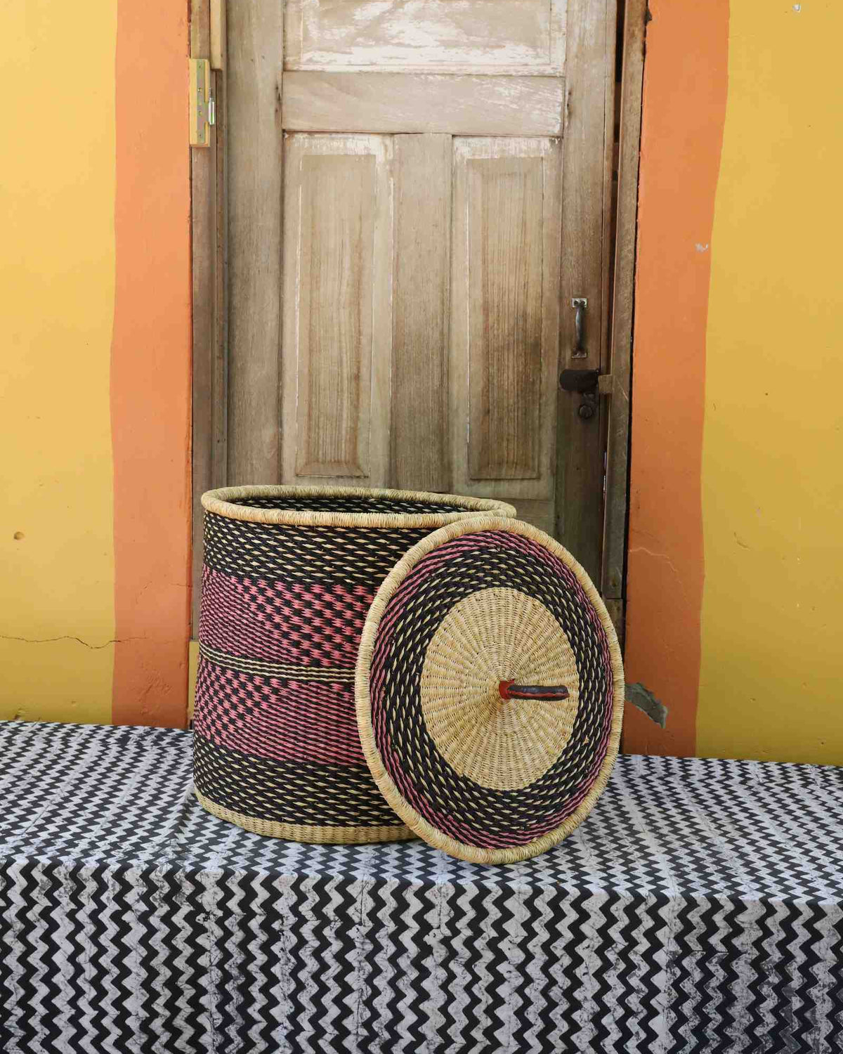 Handwoven Bolga laundry basket with lid removed, natural body with red checkered band and matching lid.
