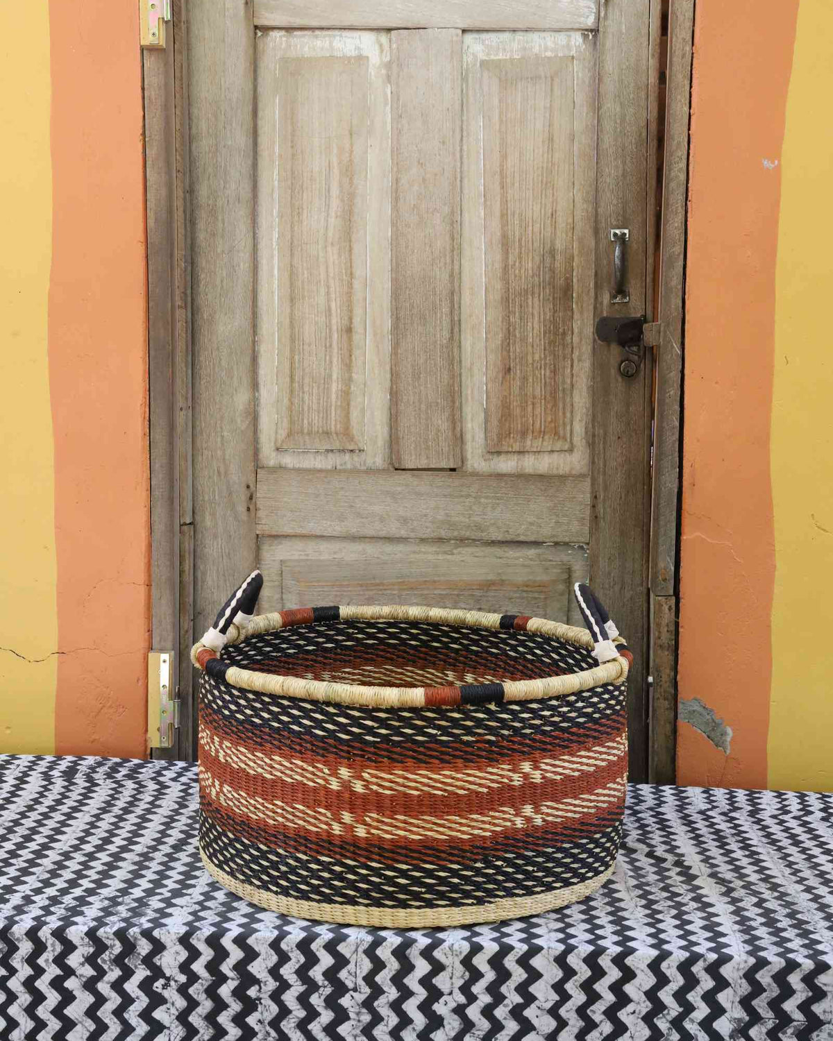 Large handwoven Bolga storage tub in natural straw with orange and black diamond weave patterns.