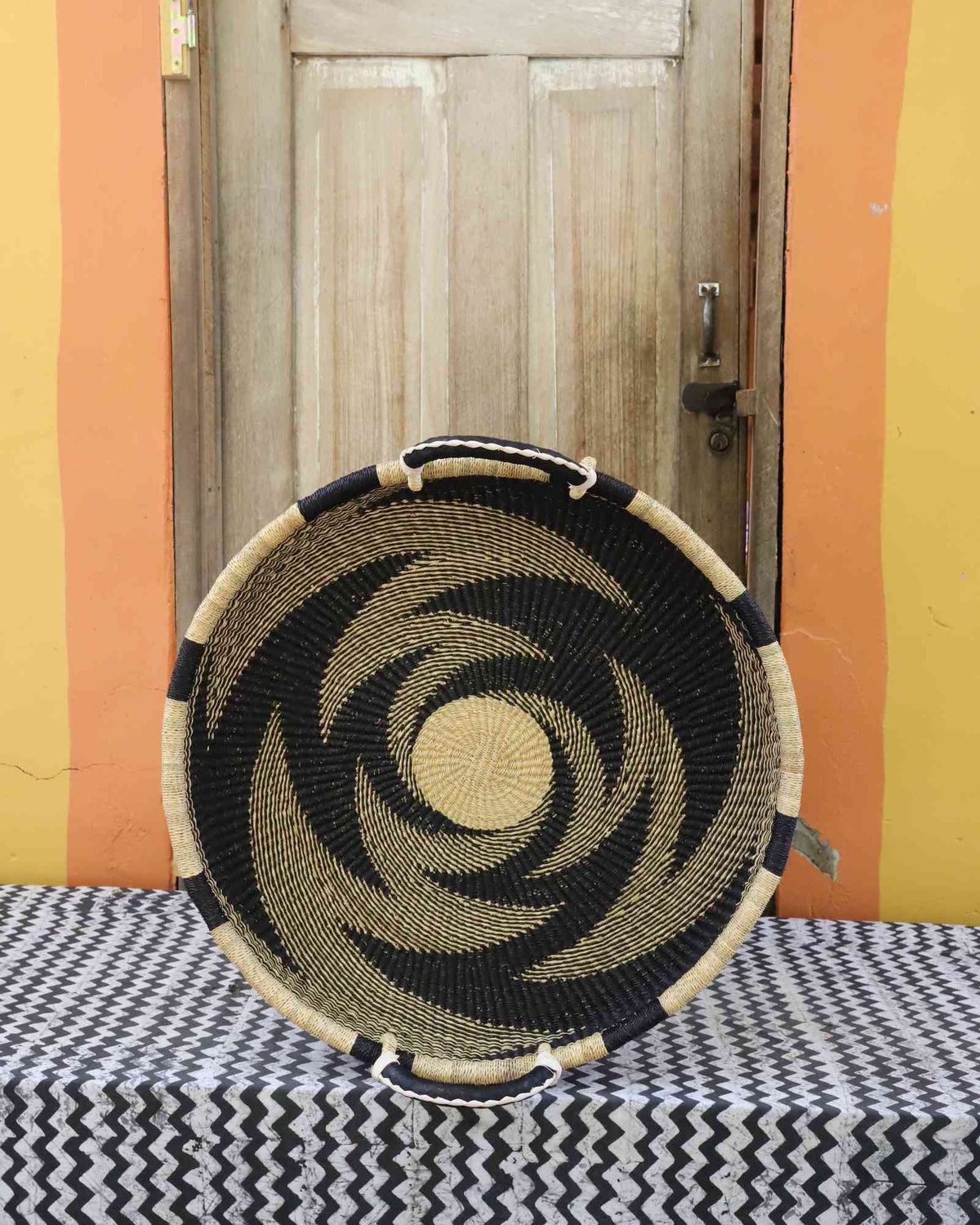 Medium handwoven Bolga wall tray disc in natural straw with a bold black pinwheel swirl.