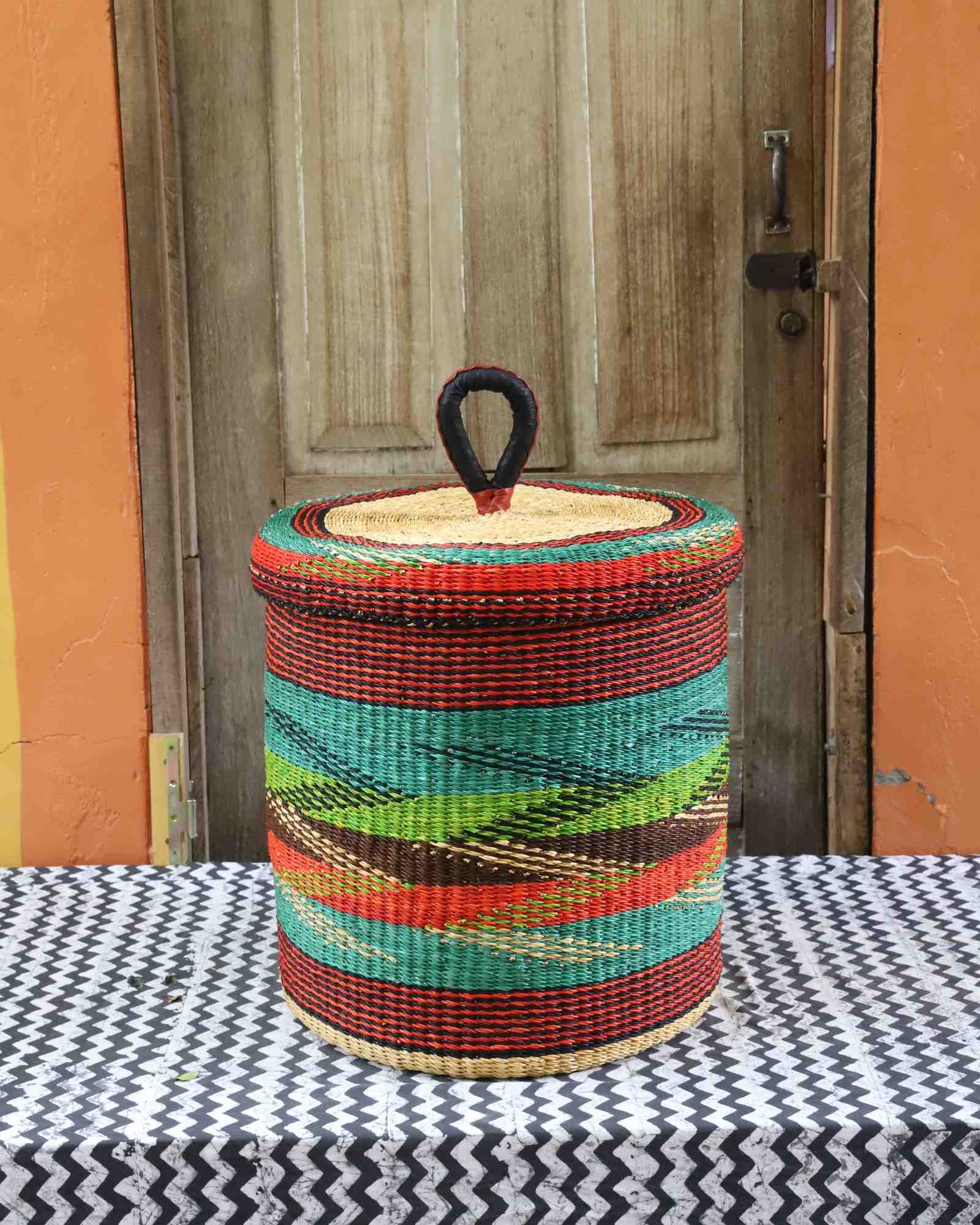 Lidded laundry basket in rust and teal wave-patterned weave, styled on a chevron cloth by a wooden door.