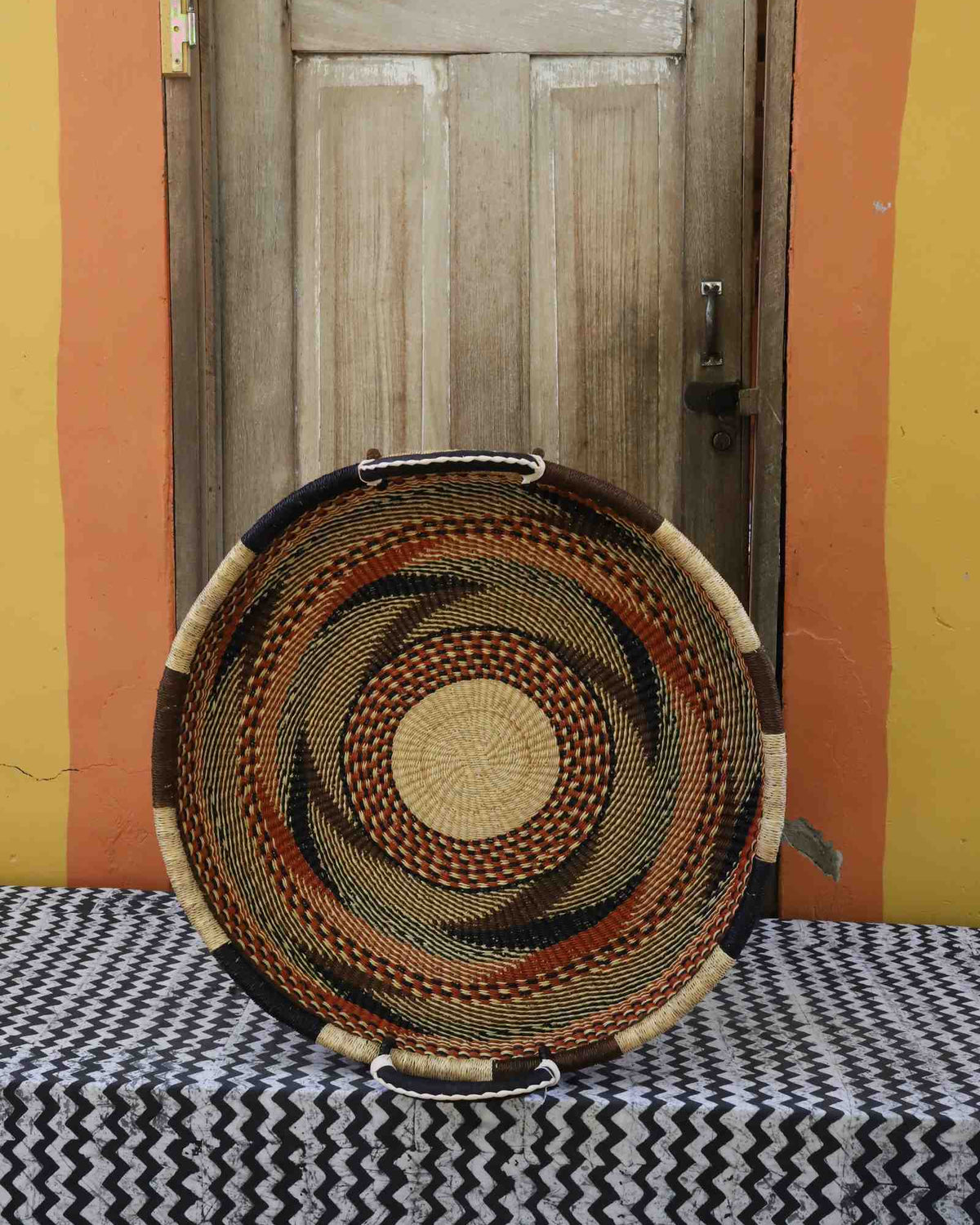 Medium handwoven Bolga wall tray disc with fine brown, black and orange concentric bands and yellow centre.