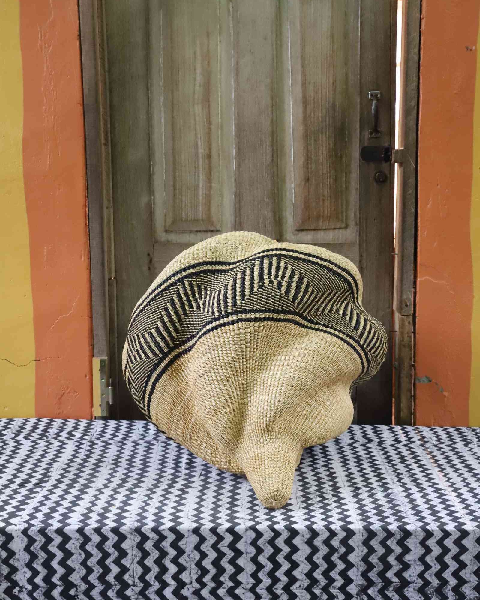 Spiral-form Bolga basket in natural straw with a bold black geometric band, angled to show its curved silhouette.