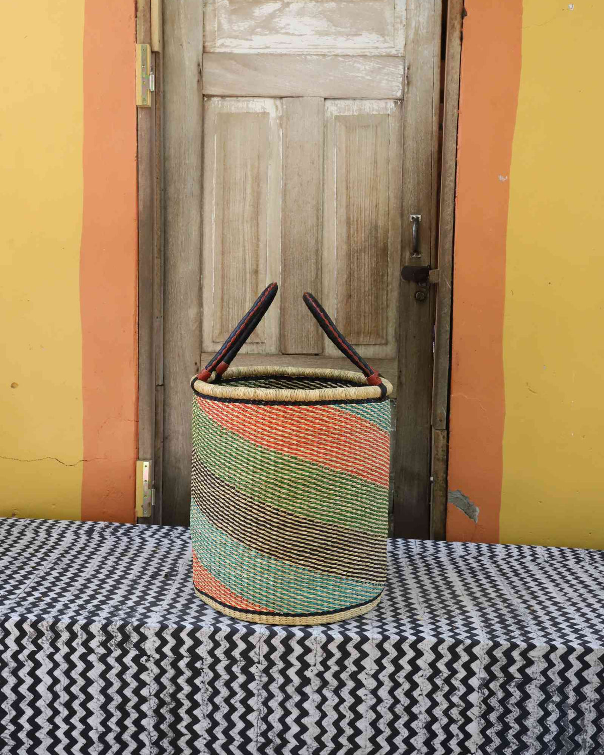 Medium handwoven open-top Bolga laundry basket in natural straw with green, orange and pink diagonal stripes.