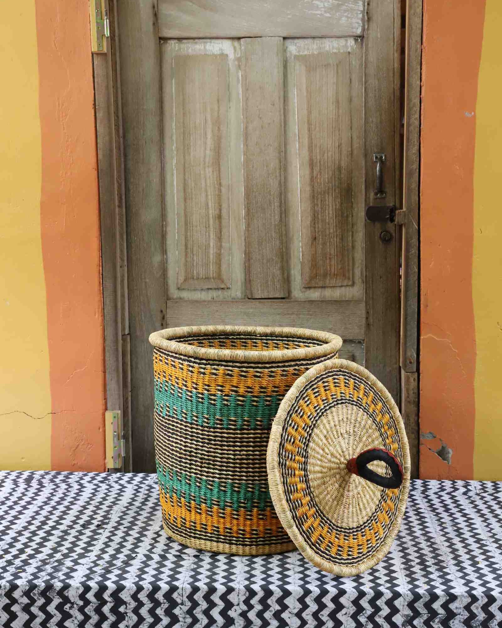 Handwoven Bolga laundry basket with lid removed, natural body with orange and teal bands and matching lid.