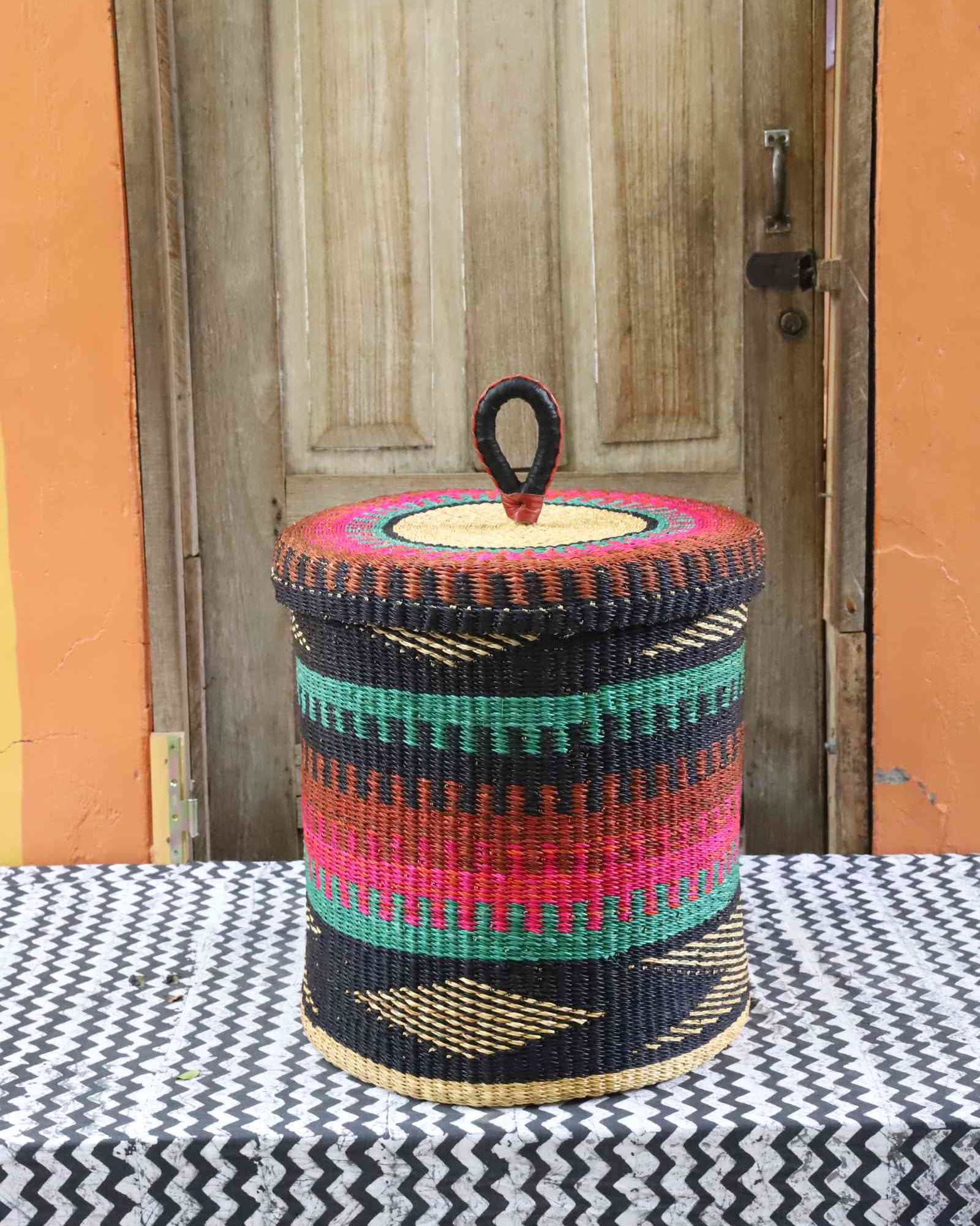 Lidded laundry basket in teal, pink and rust banded weave with a black zigzag base, styled on a chevron cloth.