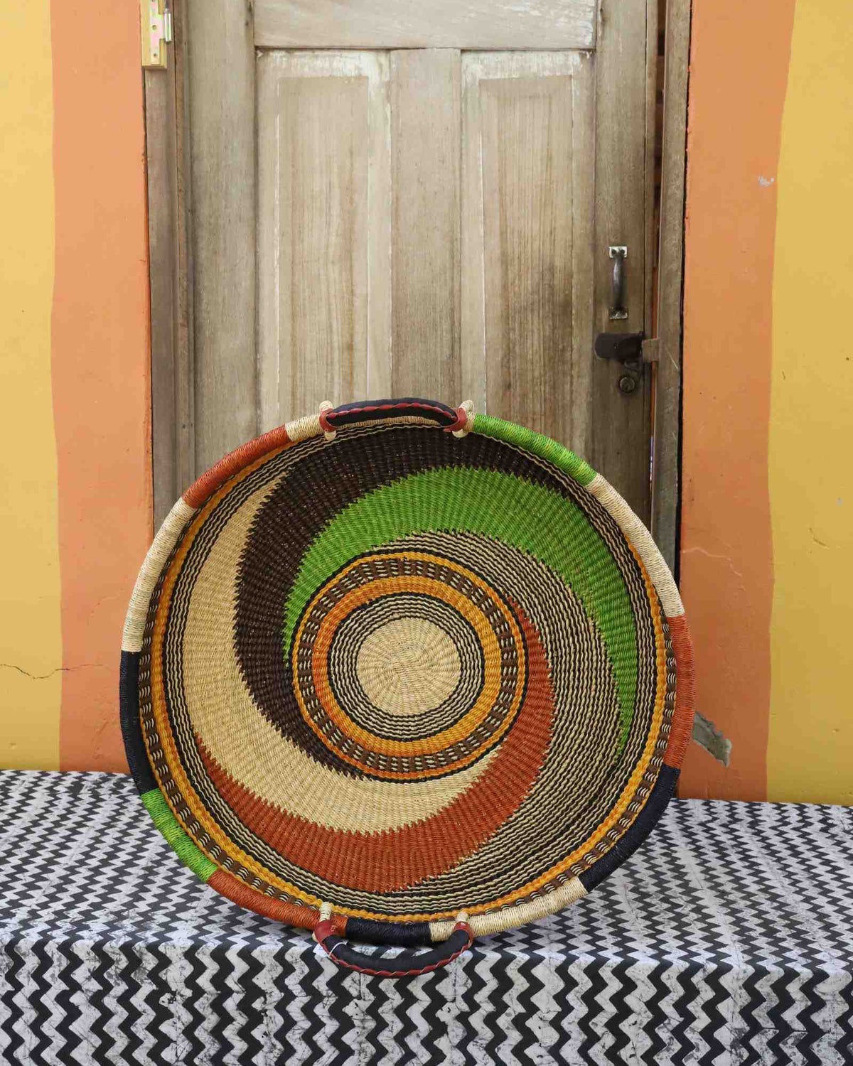 Medium handwoven Bolga wall tray disc with green, orange and black swirl and natural centre.