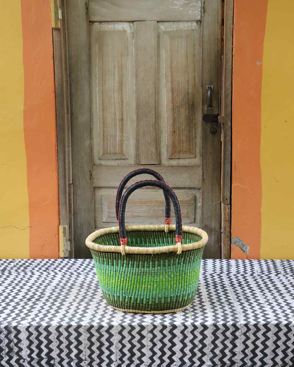 Small handwoven oval Bolga shopping basket in natural straw with green banded stripes and dark handles.