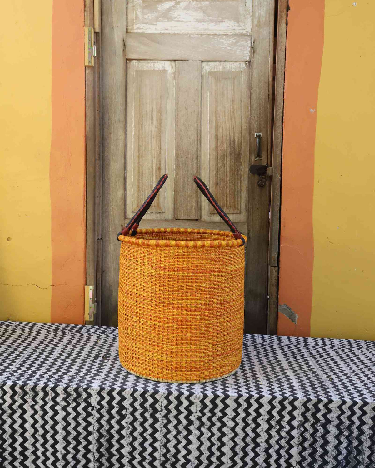 Medium handwoven open-top Bolga laundry basket dyed bold orange with a plain woven body.