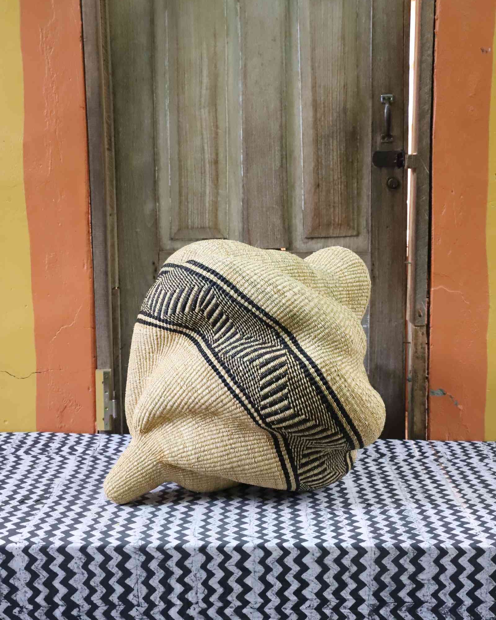 Natural straw Bolga basket in a coiled spiral shape with a black geometric band, shown from a rear angle on a tablecloth.