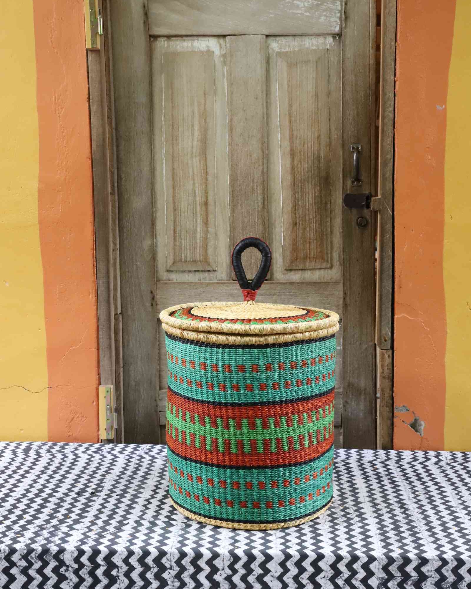 Handwoven Bolga laundry basket with coiled rim and lid in natural straw with teal, red and green banded stripes.
