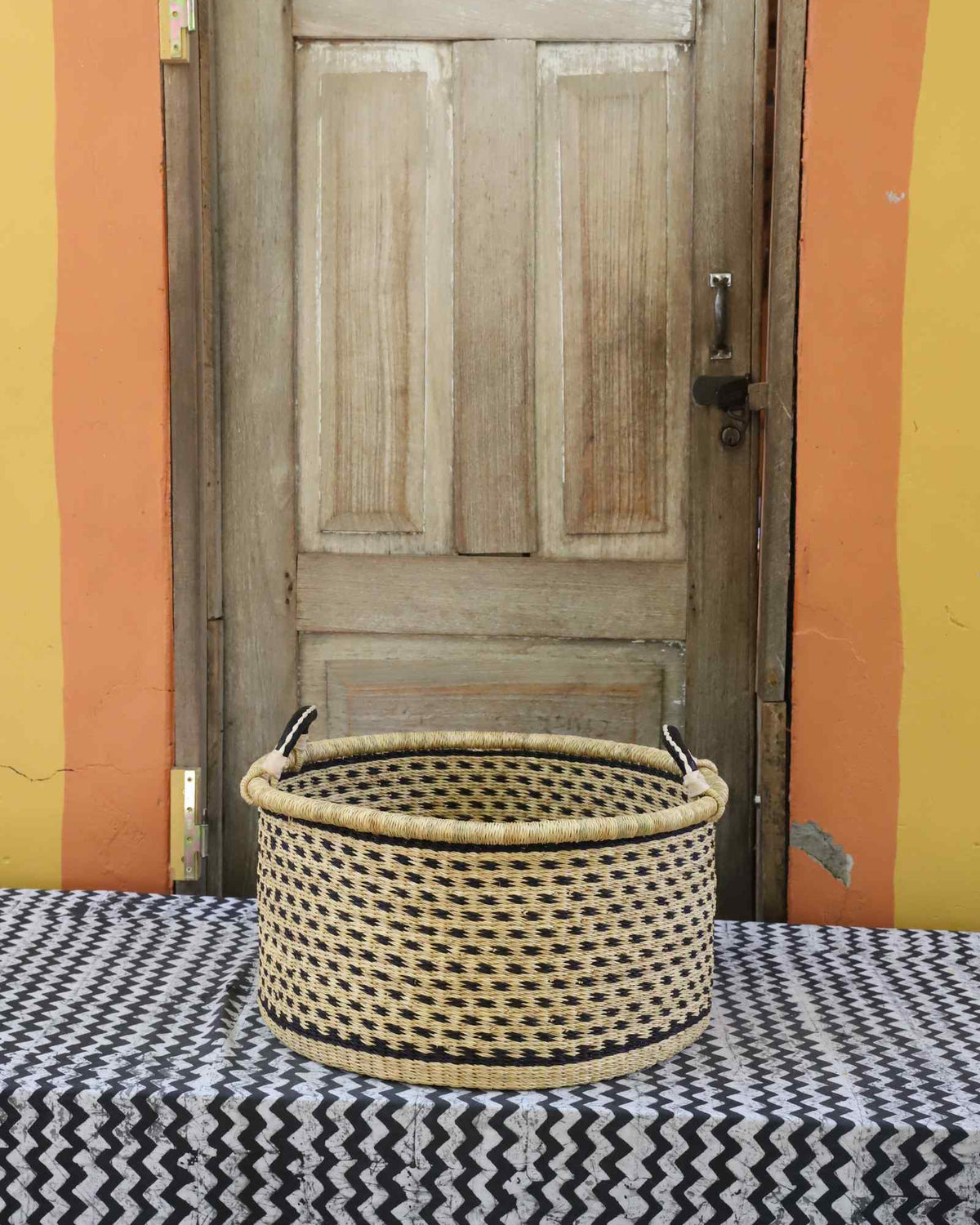 Medium handwoven Bolga storage tub in plain natural straw with a fine diagonal weave and dark handles.