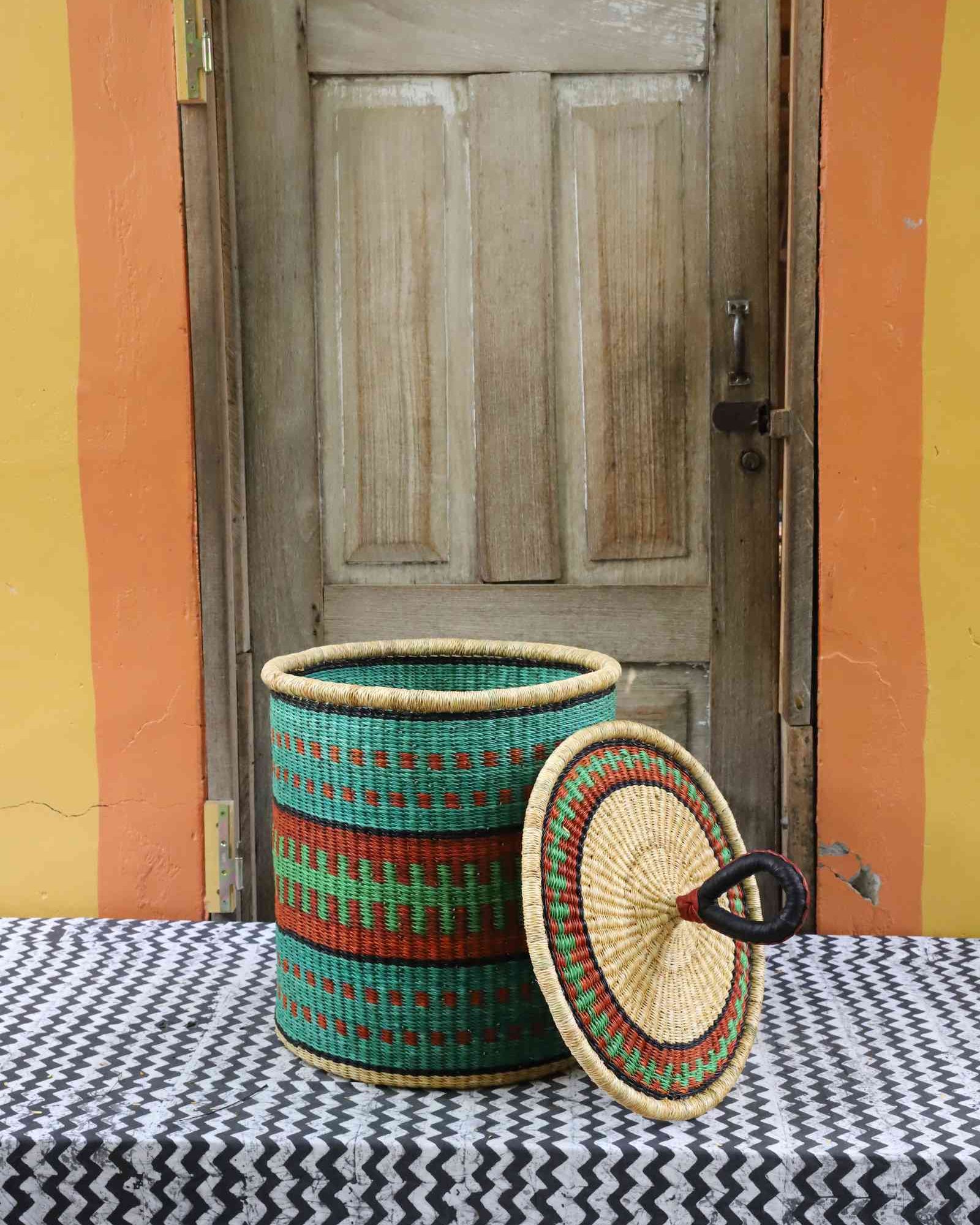 Handwoven Bolga laundry basket with lid removed, showing teal, red and green banded body and lid.
