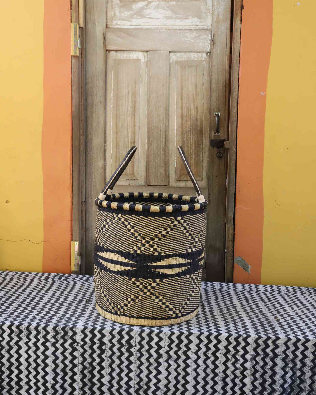 Medium handwoven open-top Bolga laundry basket in natural straw with black wave and wing motifs.