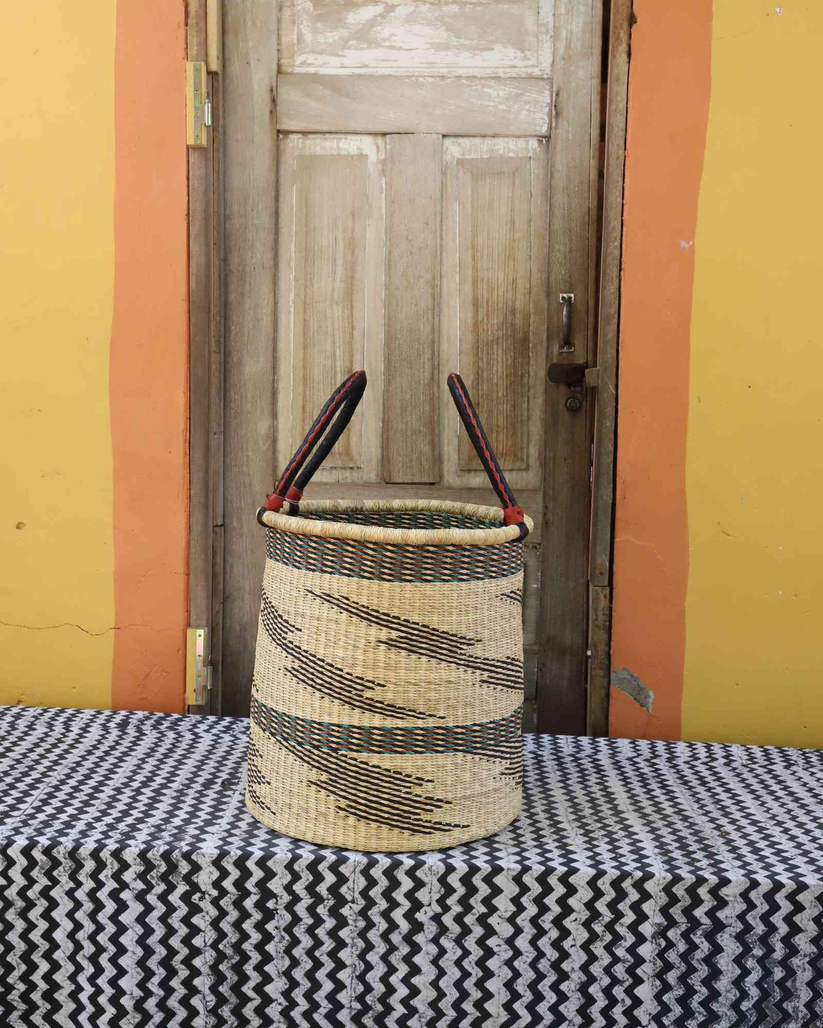 Medium handwoven open-top Bolga laundry basket in natural straw with scattered black wave motifs.