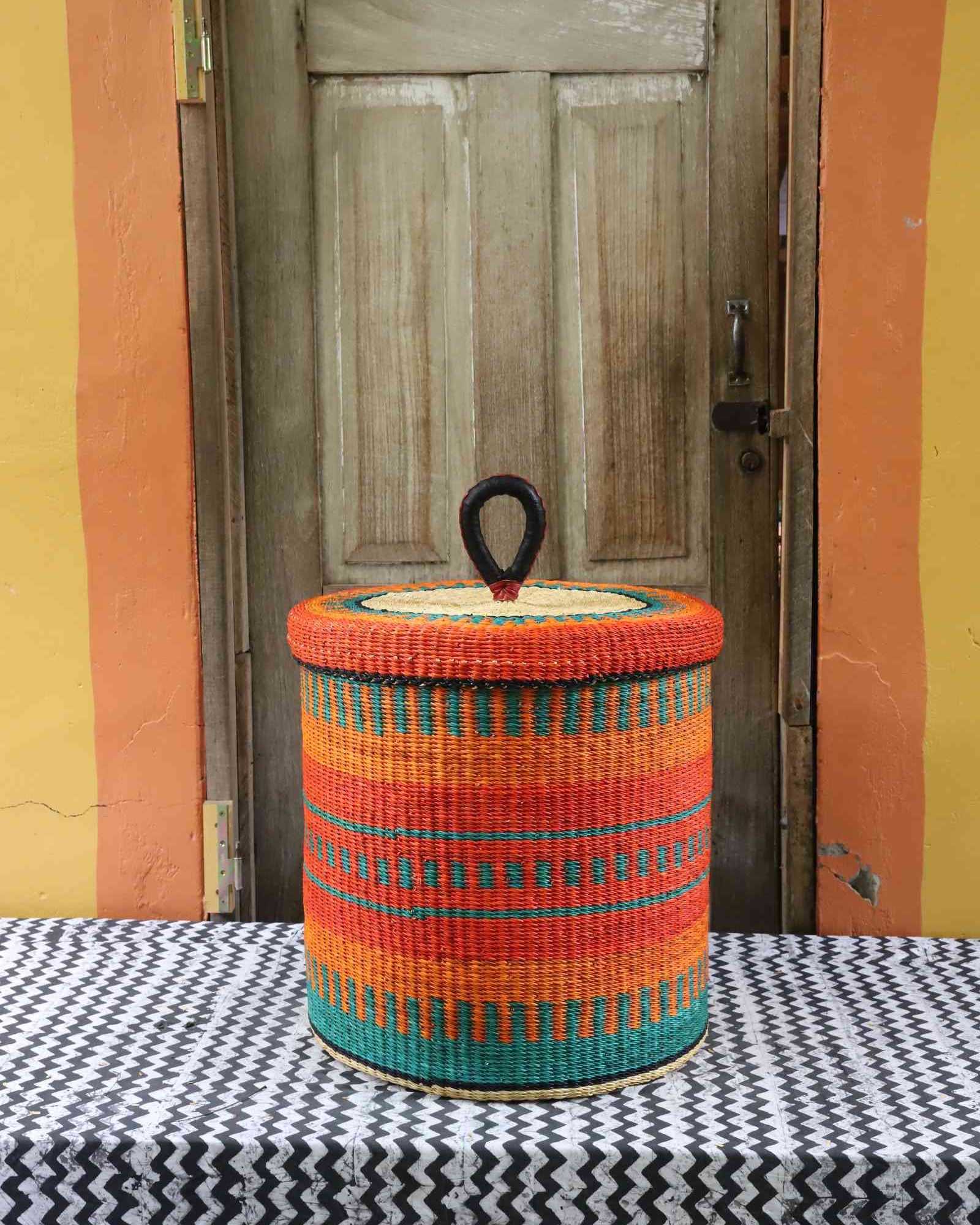 Handwoven Bolga laundry basket with lid in orange elephant grass with teal horizontal stripes.
