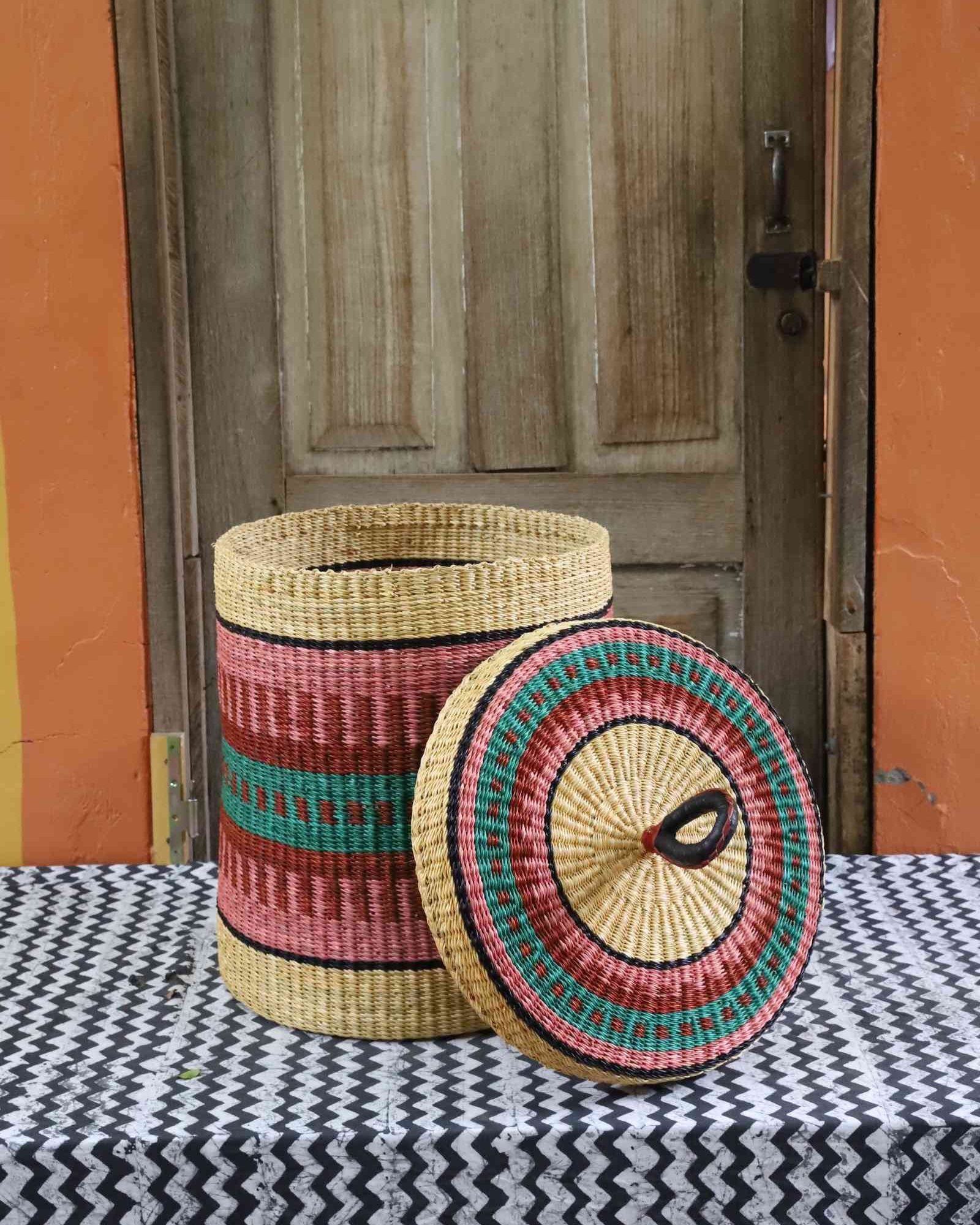 Lidded laundry basket in natural straw with pink and teal striped banding, lid resting alongside on a chevron cloth.