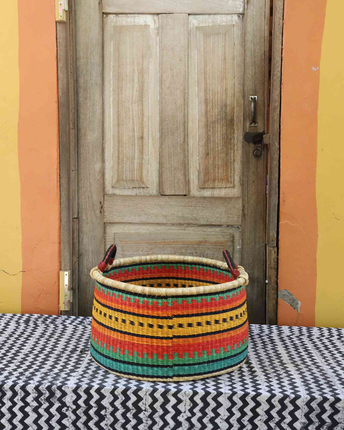 Medium handwoven Bolga storage tub in dyed green with orange and yellow banded stripes and dark handles.