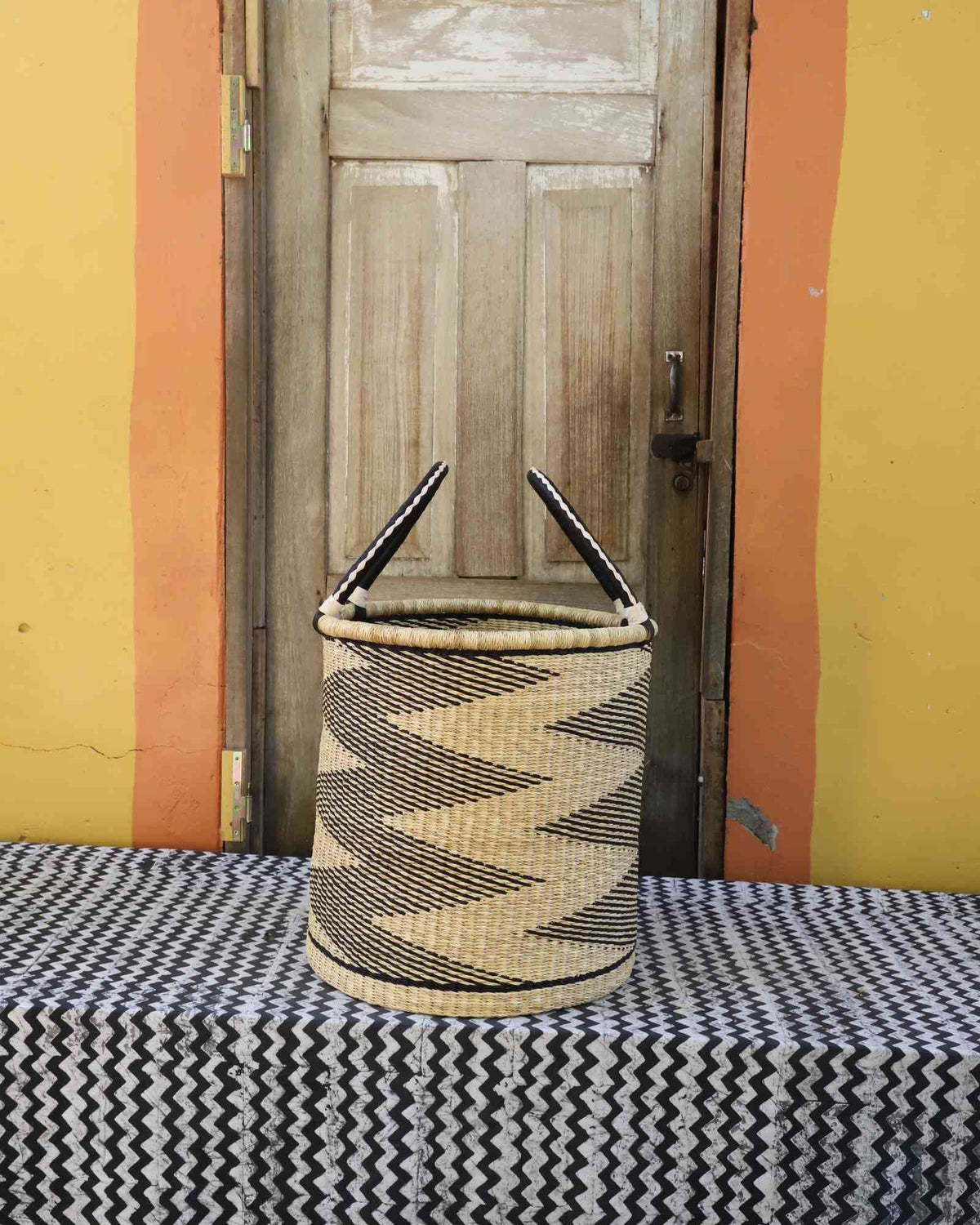 Medium handwoven open-top Bolga laundry basket in natural straw with black jagged sawtooth stripes.