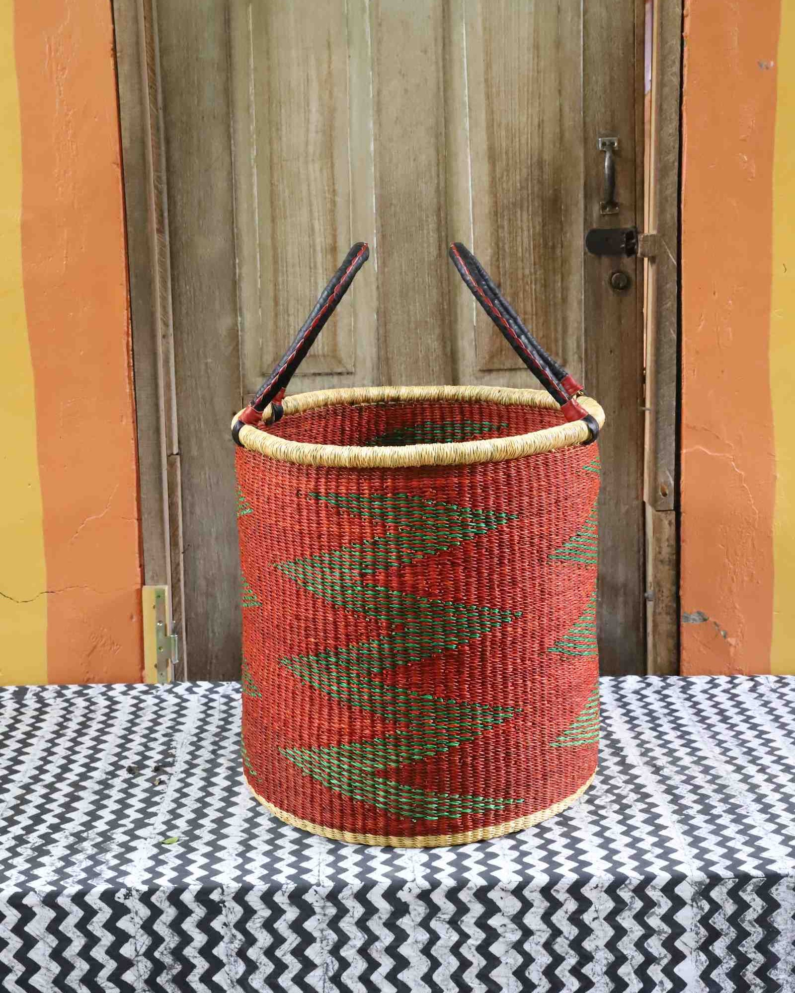 Large open laundry basket in red and green zigzag weave with arched handles, styled on a chevron cloth.