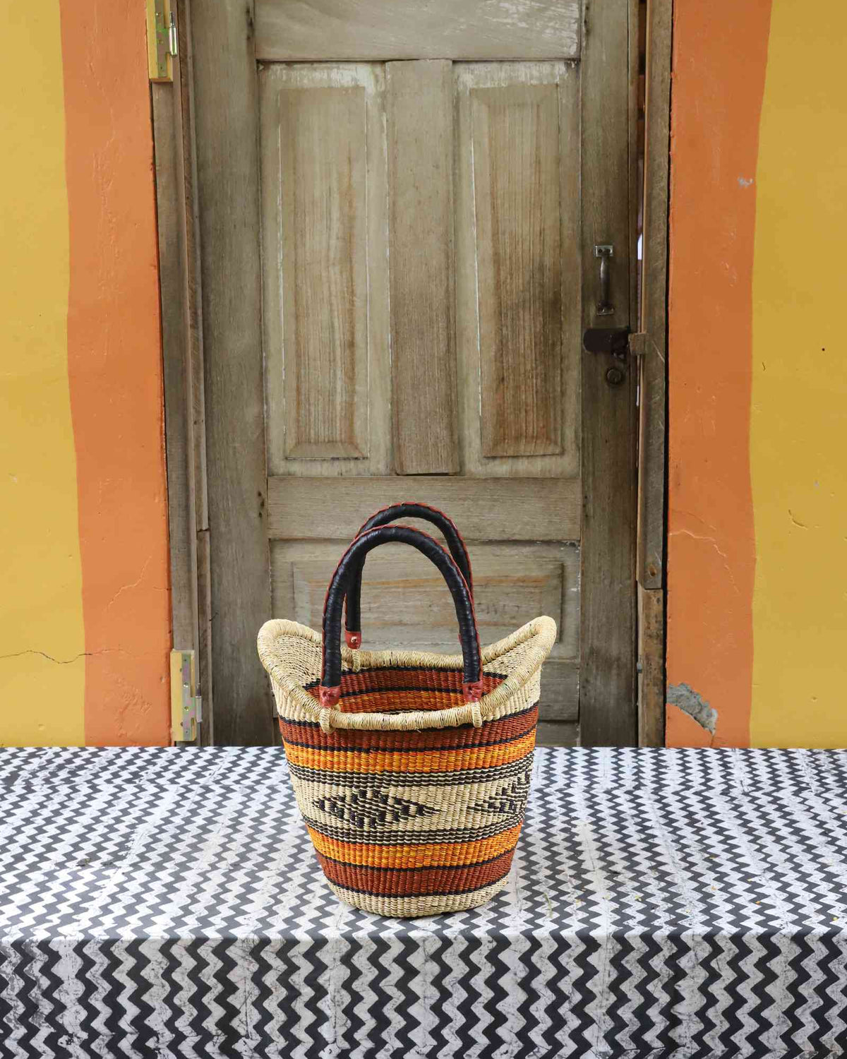 Small handwoven Nyariga Bolga shopping basket in orange and red fine banded stripes with dark handles.