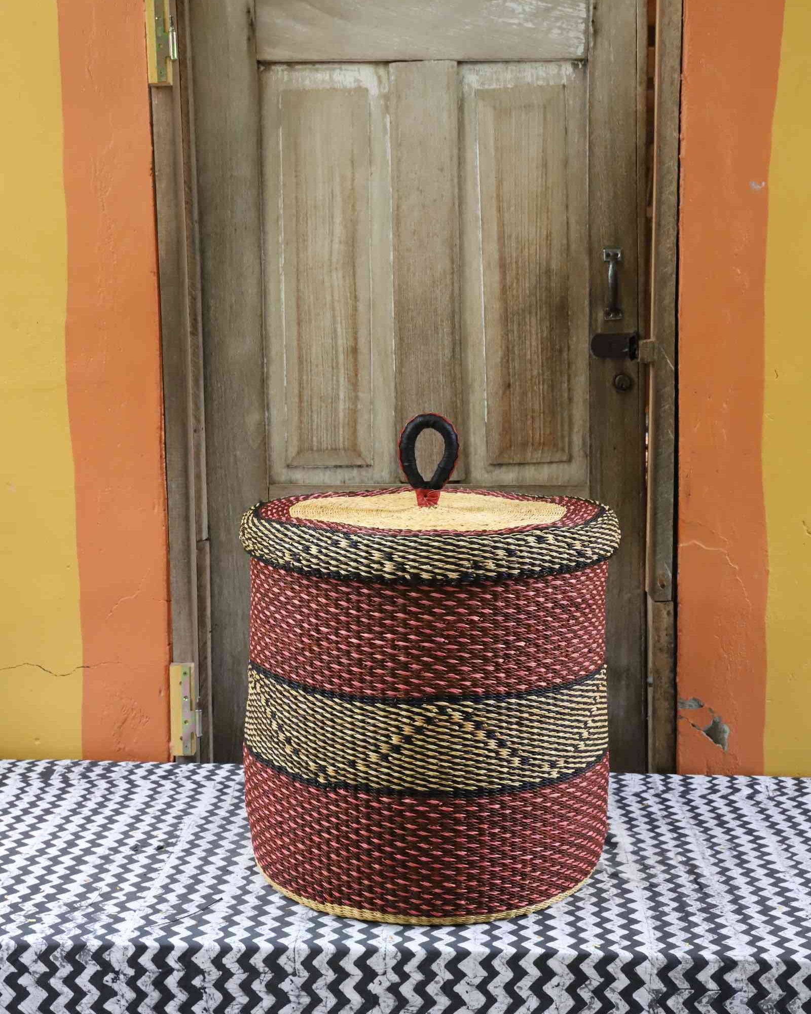 Handwoven Bolga laundry basket with lid in deep red with a black woven accent band and natural straw lid.