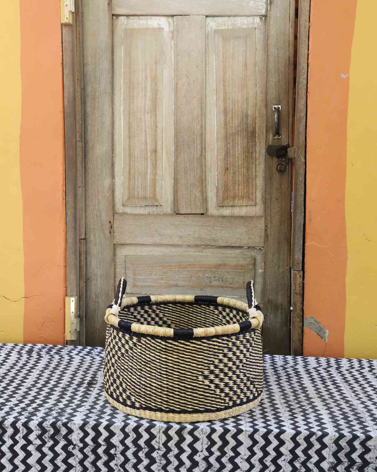 Small handwoven Bolga storage tub in natural straw with fine checker weave and dark leather-wrapped rim.