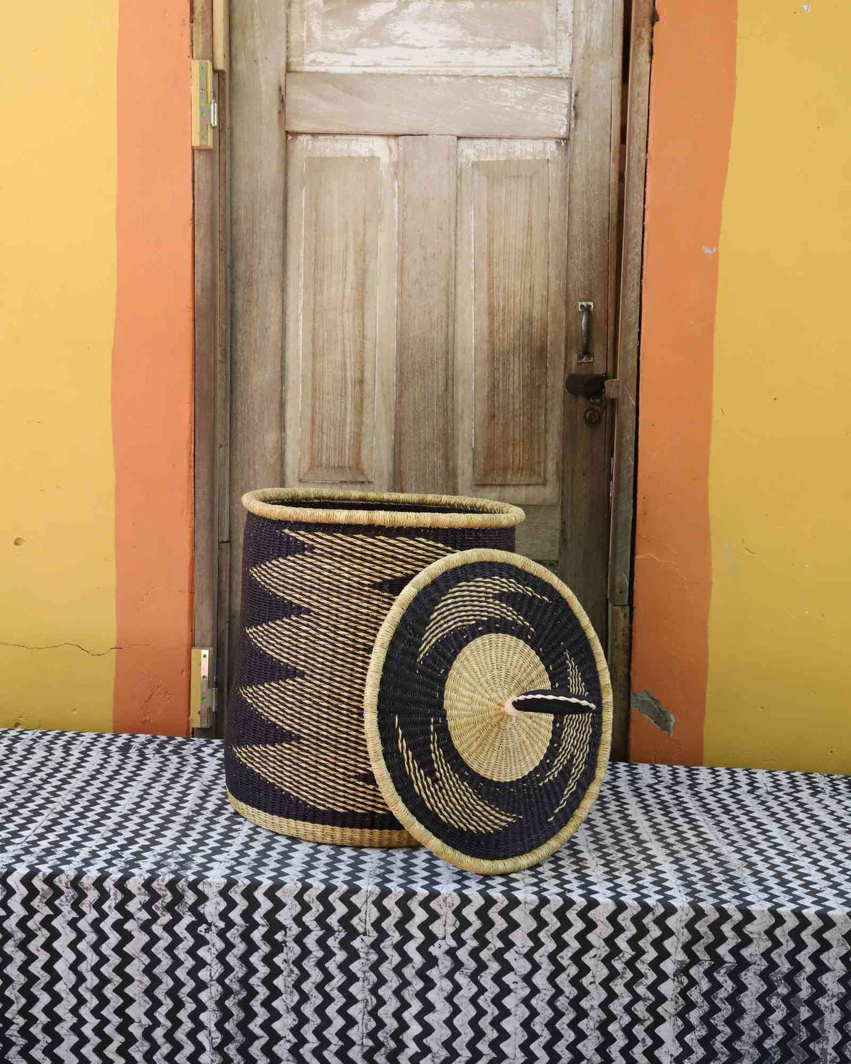 Handwoven Bolga laundry basket with lid removed, natural body with black zigzag and coiled rim lid.