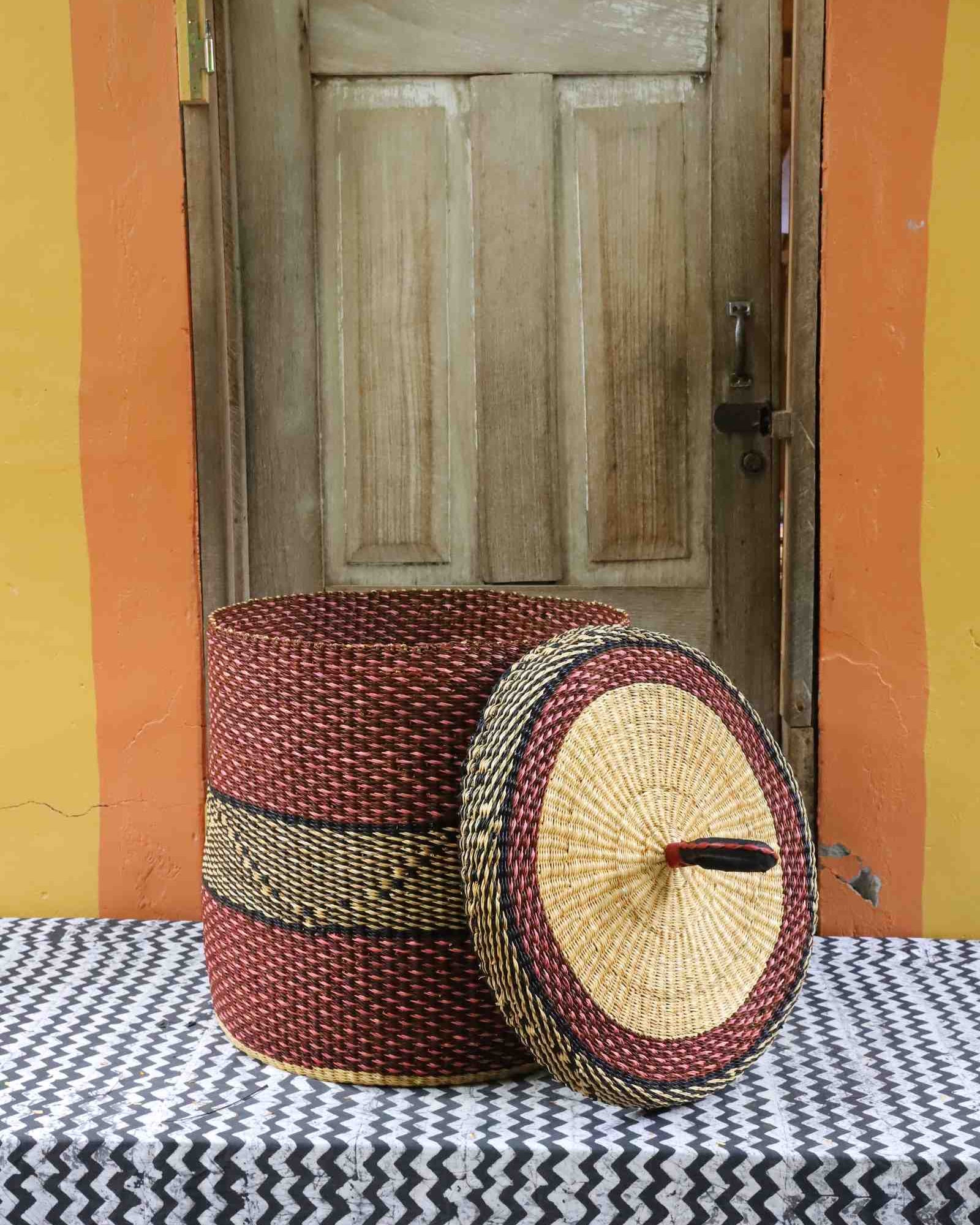 Handwoven Bolga laundry basket with lid removed, showing a deep red body with black accent and natural lid.