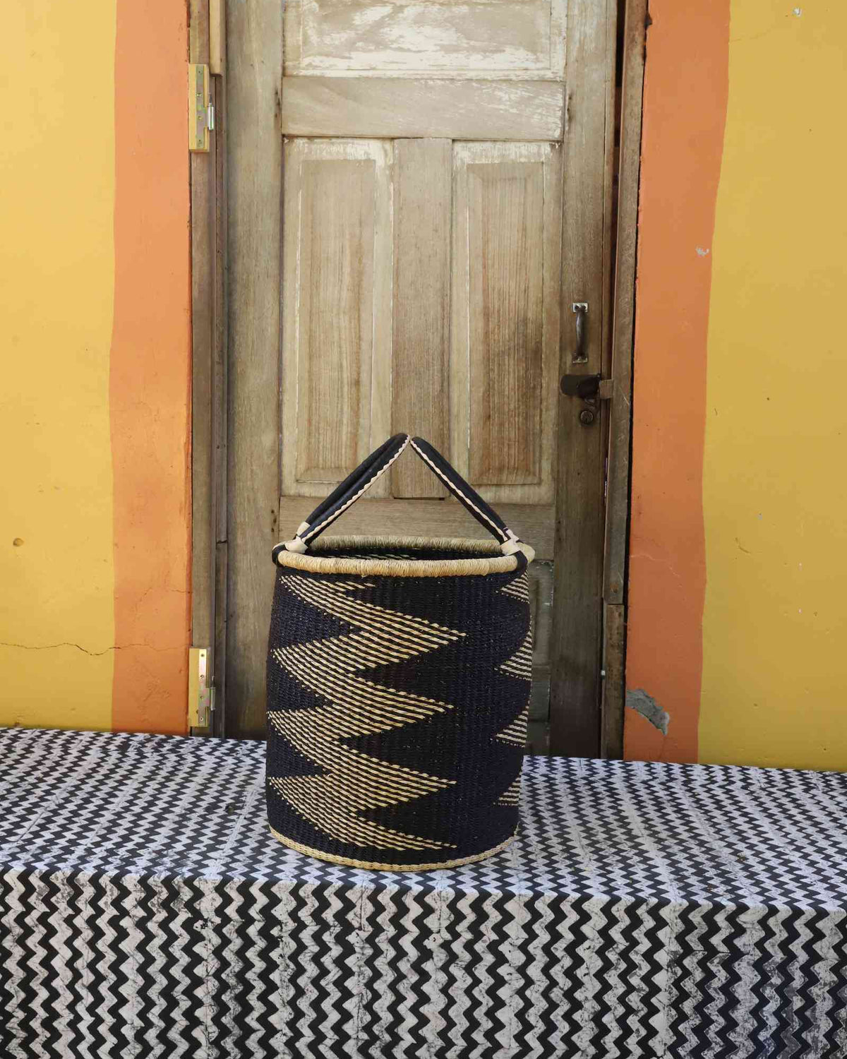 Small handwoven open-top Bolga laundry basket in natural straw with a bold black zigzag pattern.